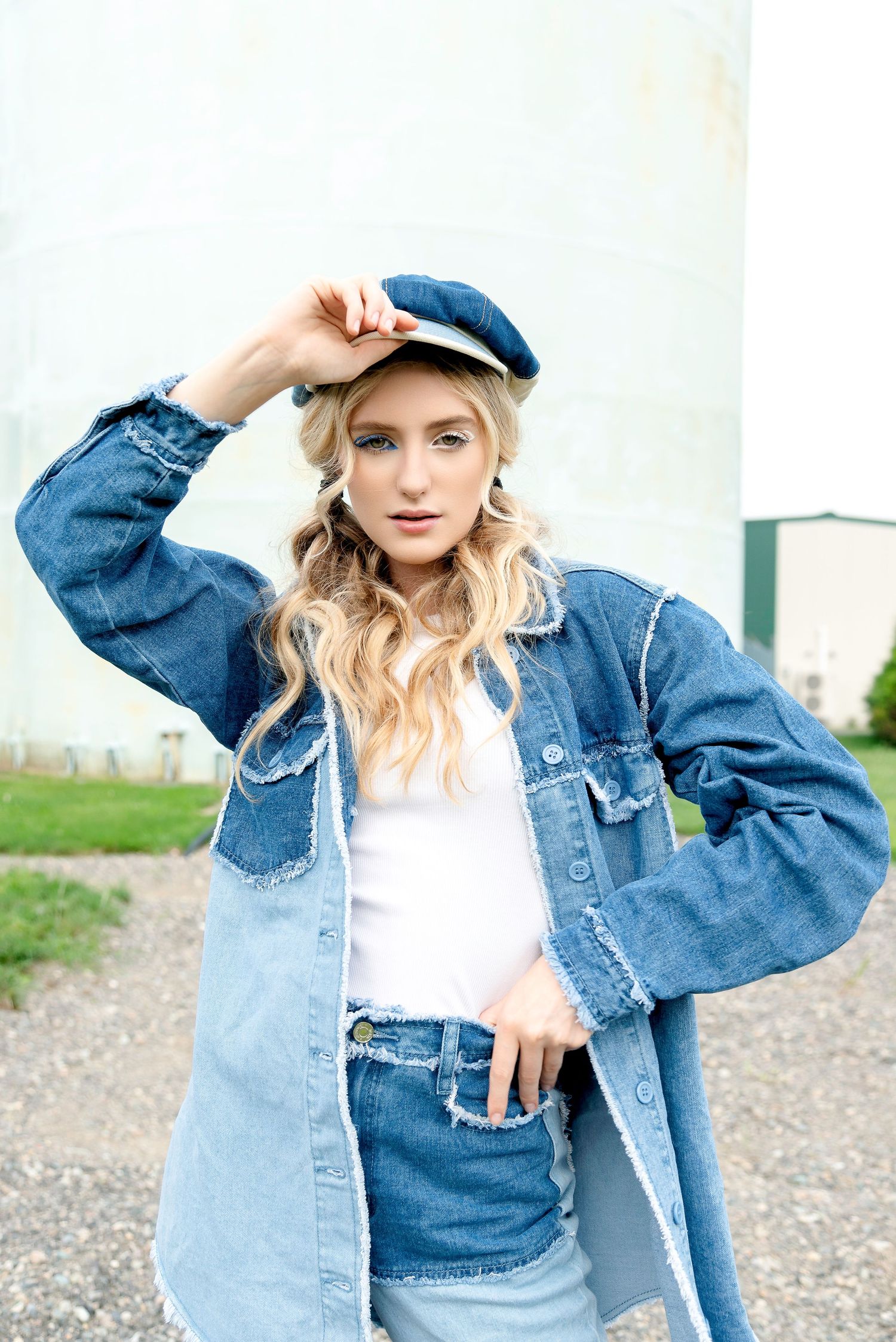 Stylish denim on denim outfit featuring a blue jean jacket, white top, and matching newsboy cap in outdoor setting.
