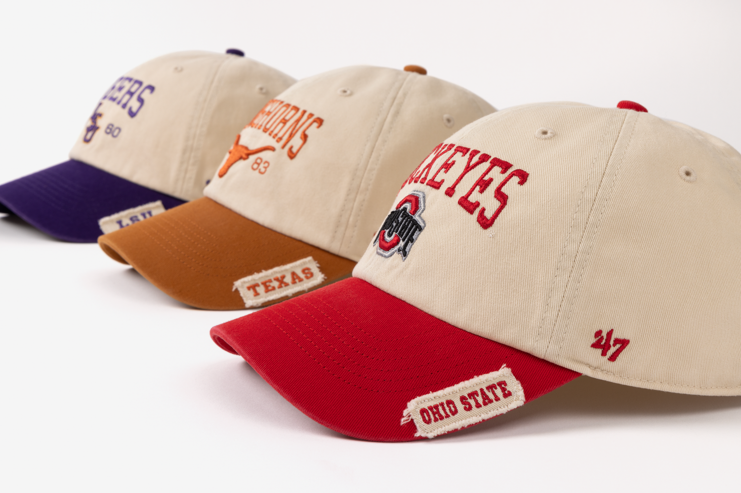 Collection of tan baseball caps with red brims and sports team logos displayed in a row.
