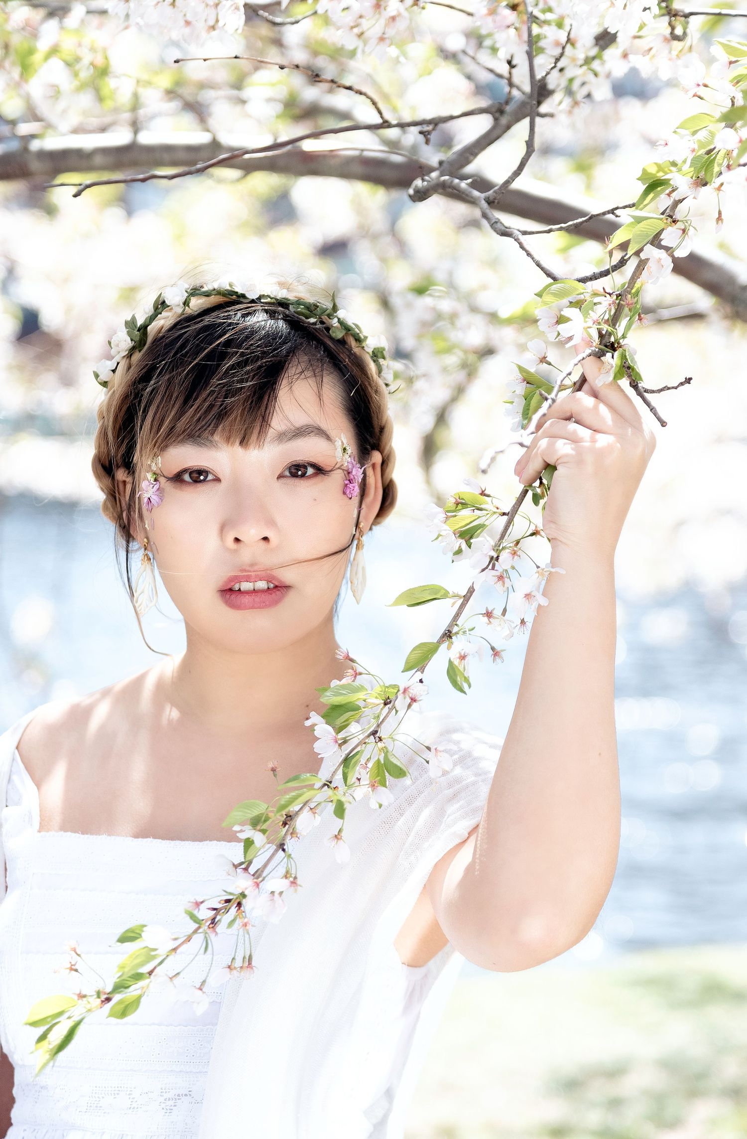 A person poses playfully under blooming cherry blossom branches against a bright spring background.