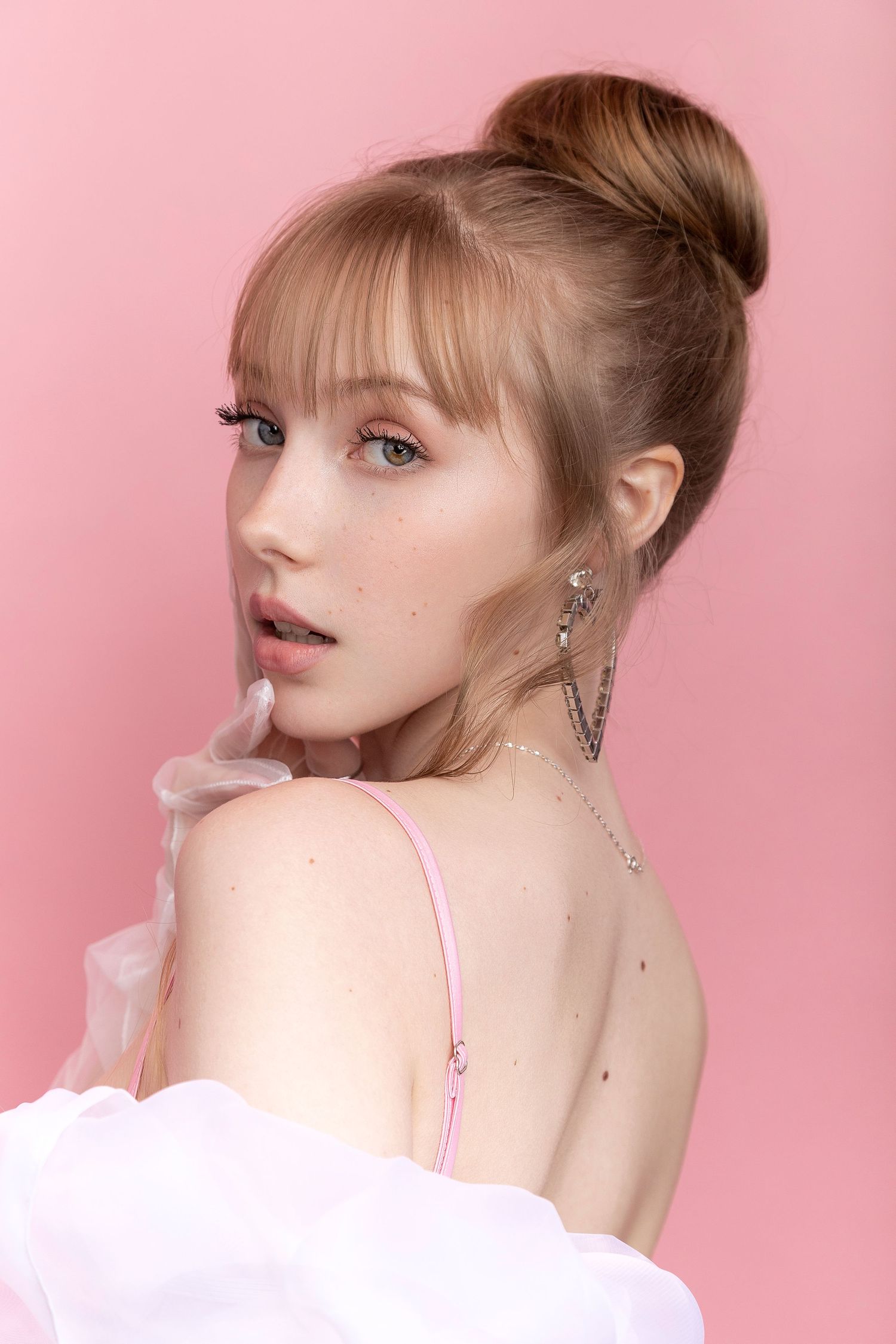 Fashion portrait with pink background showing elegant updo hairstyle and delicate jewelry styling.