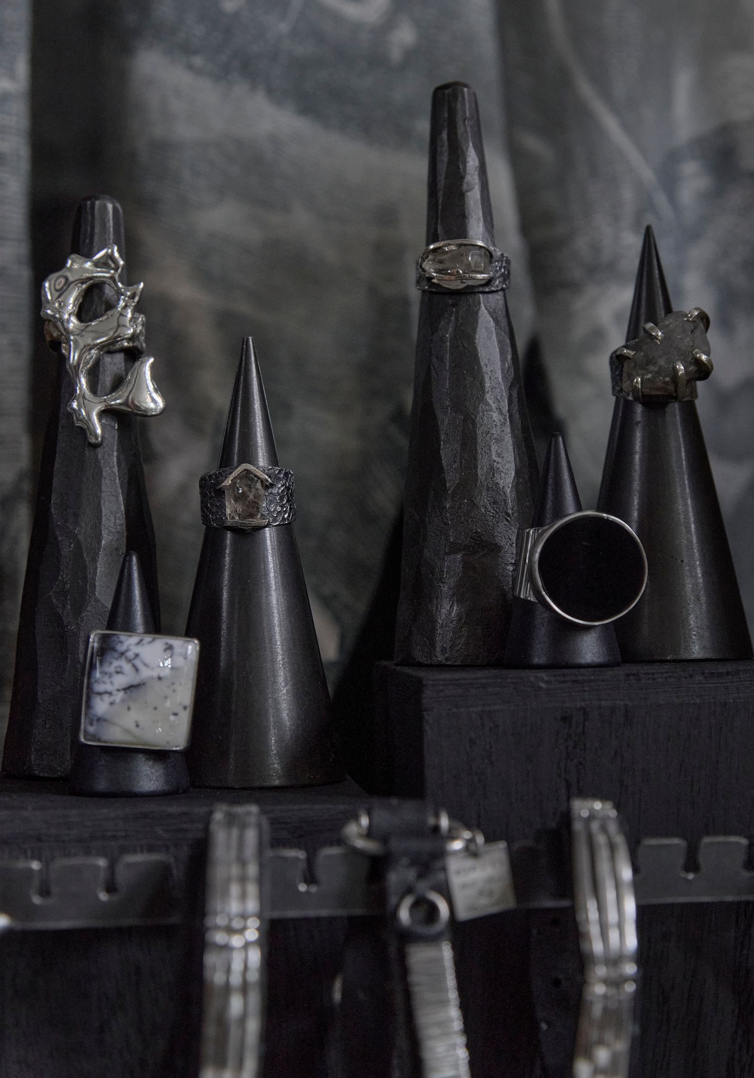 Dark cone ring displays showcase gothic silver rings with unique designs on a moody black jewelry stand.