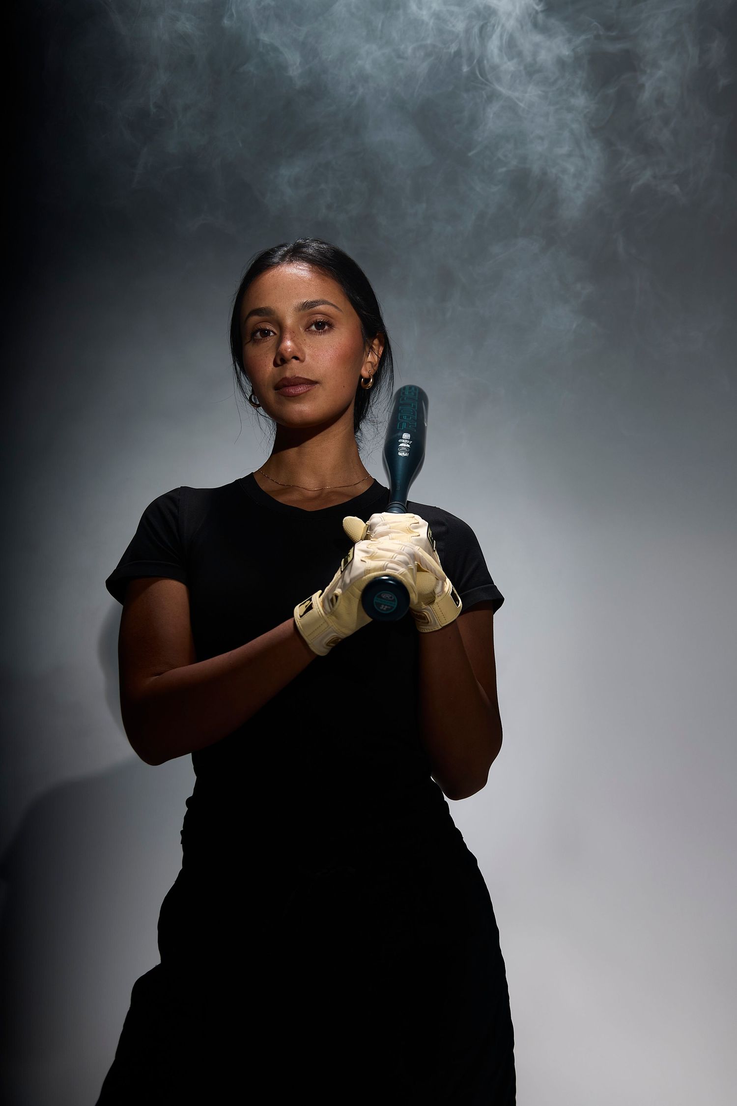 Dramatic portrait of someone in black attire holding a hairdryer against smoky background with moody lighting.