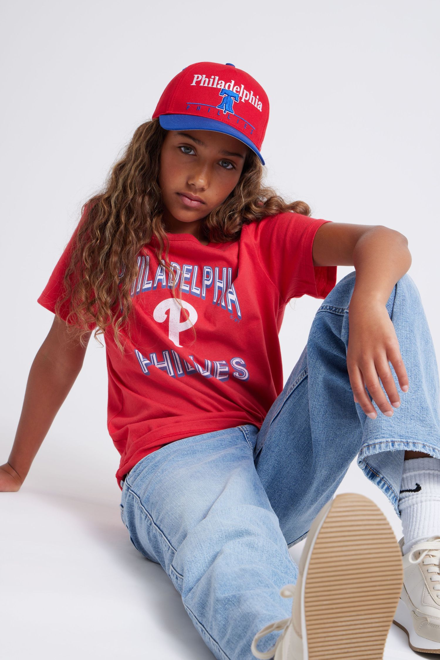 Philadelphia Phillies fan wearing red team t-shirt, baseball cap and jeans poses against white background.