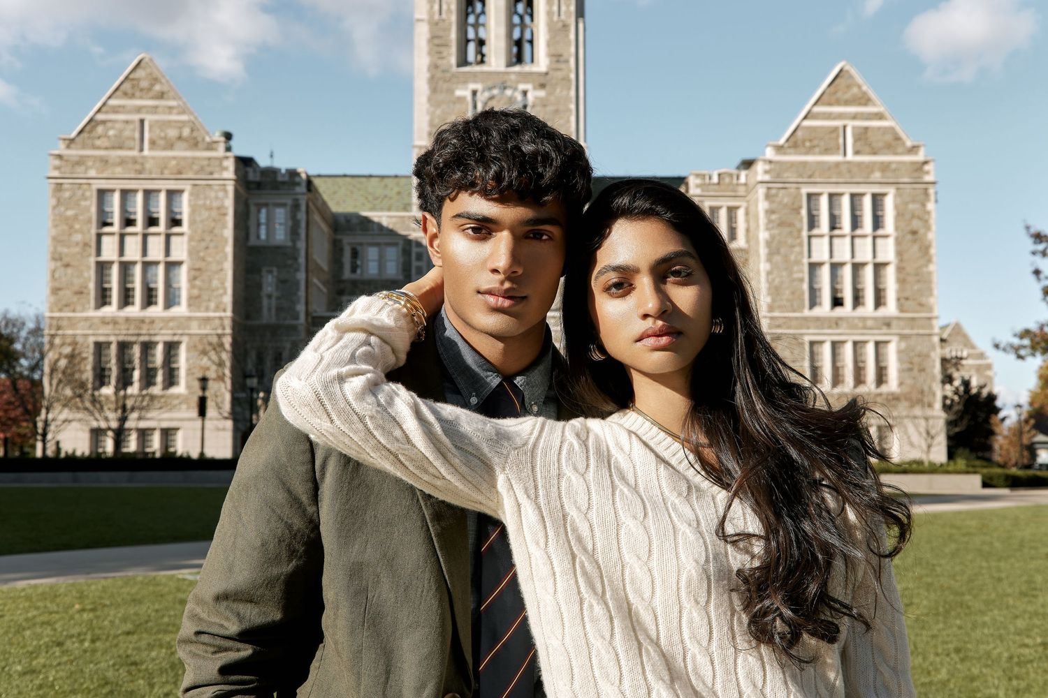 Two people stand together in front of a gothic stone building with arched windows and towers on a sunny day.