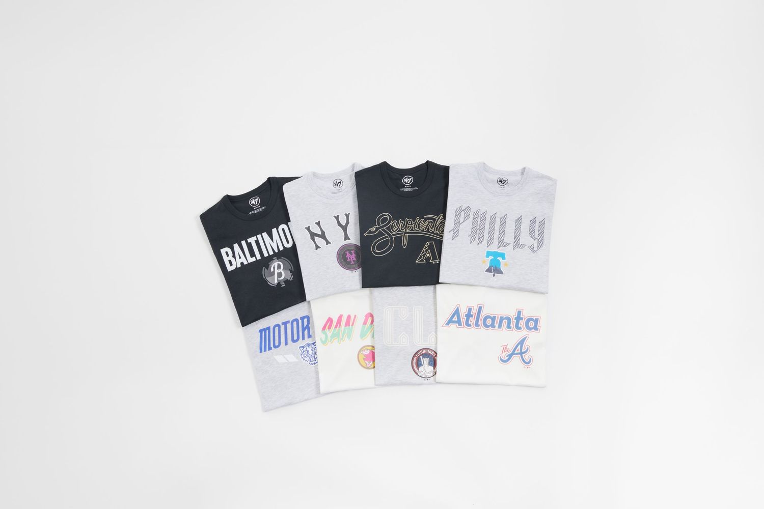 A collection of graphic t-shirts featuring city names and designs laid out in a row on a white background.