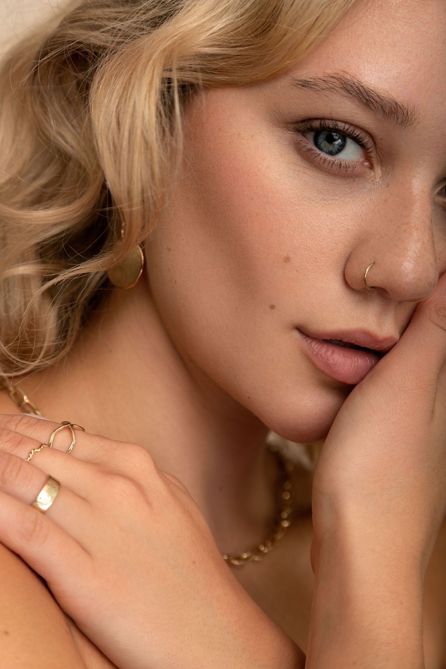 Close-up fashion portrait showing delicate gold jewelry and natural makeup in warm lighting.