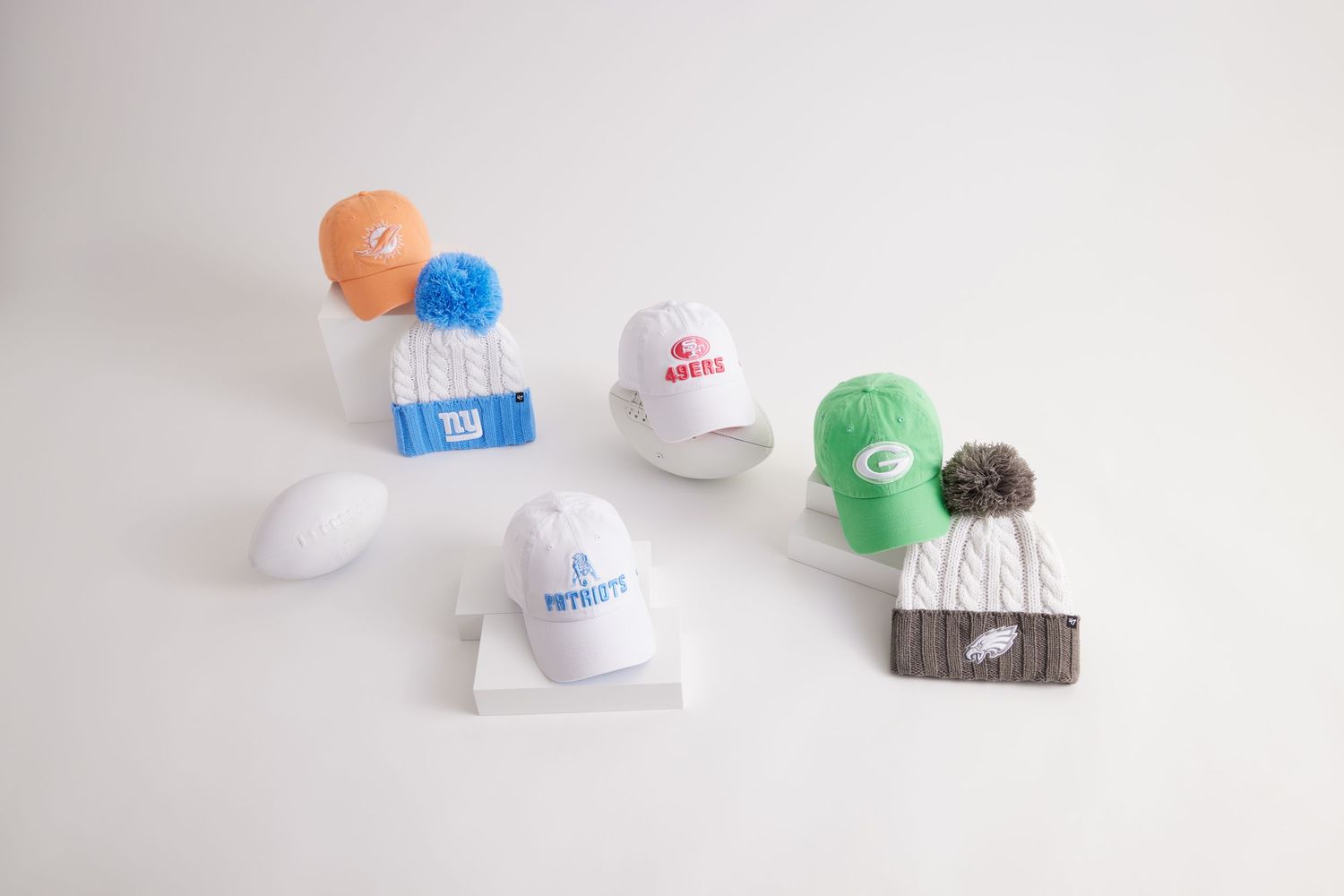 A collection of white baseball caps with colorful pom poms and embroidered designs displayed on a light background.