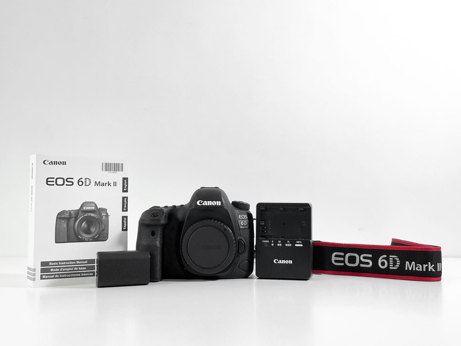 Canon EOS 6D Mark II DSLR camera body with manual, battery, and red strap on white background.