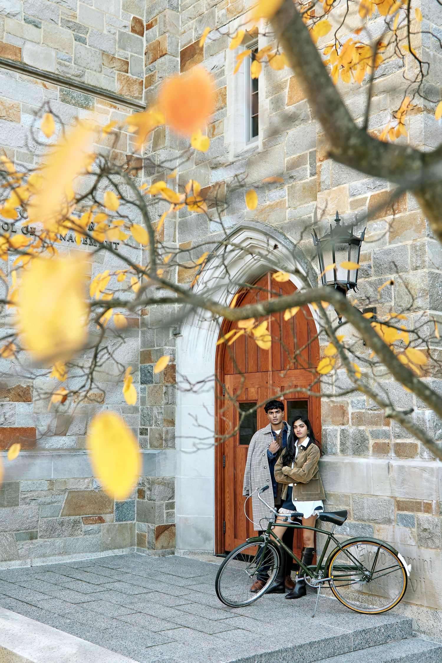 Autumn scene with vintage bicycle leaning against stone wall with wooden doors and golden leaves in foreground.