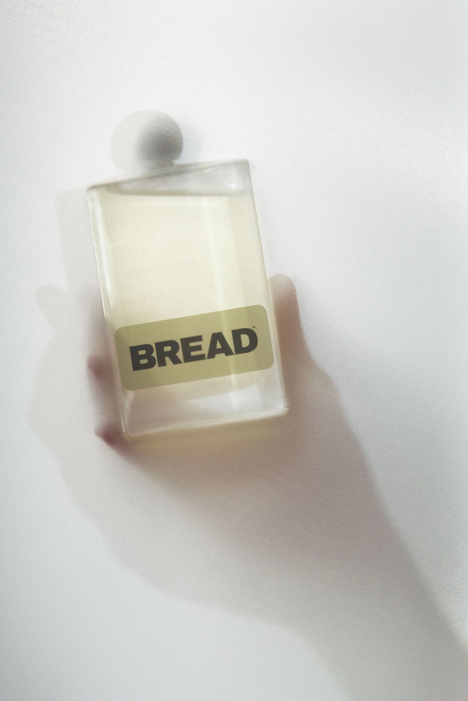 A minimalist perfume bottle labeled 'BREAD' containing pale yellow liquid against a white background with soft shadows.