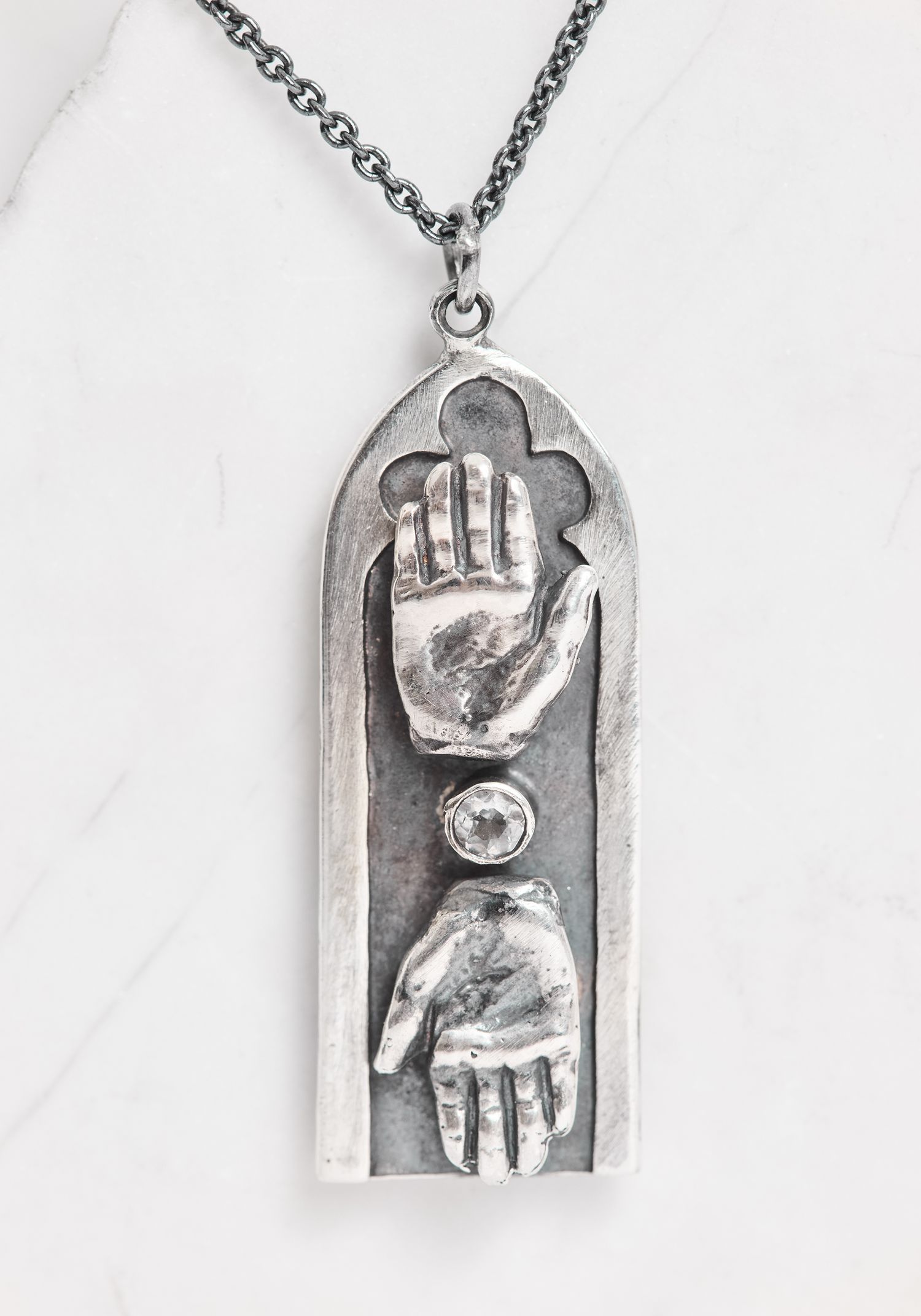 Silver pendant necklace featuring two raised hands facing each other within an arched frame on a chain.
