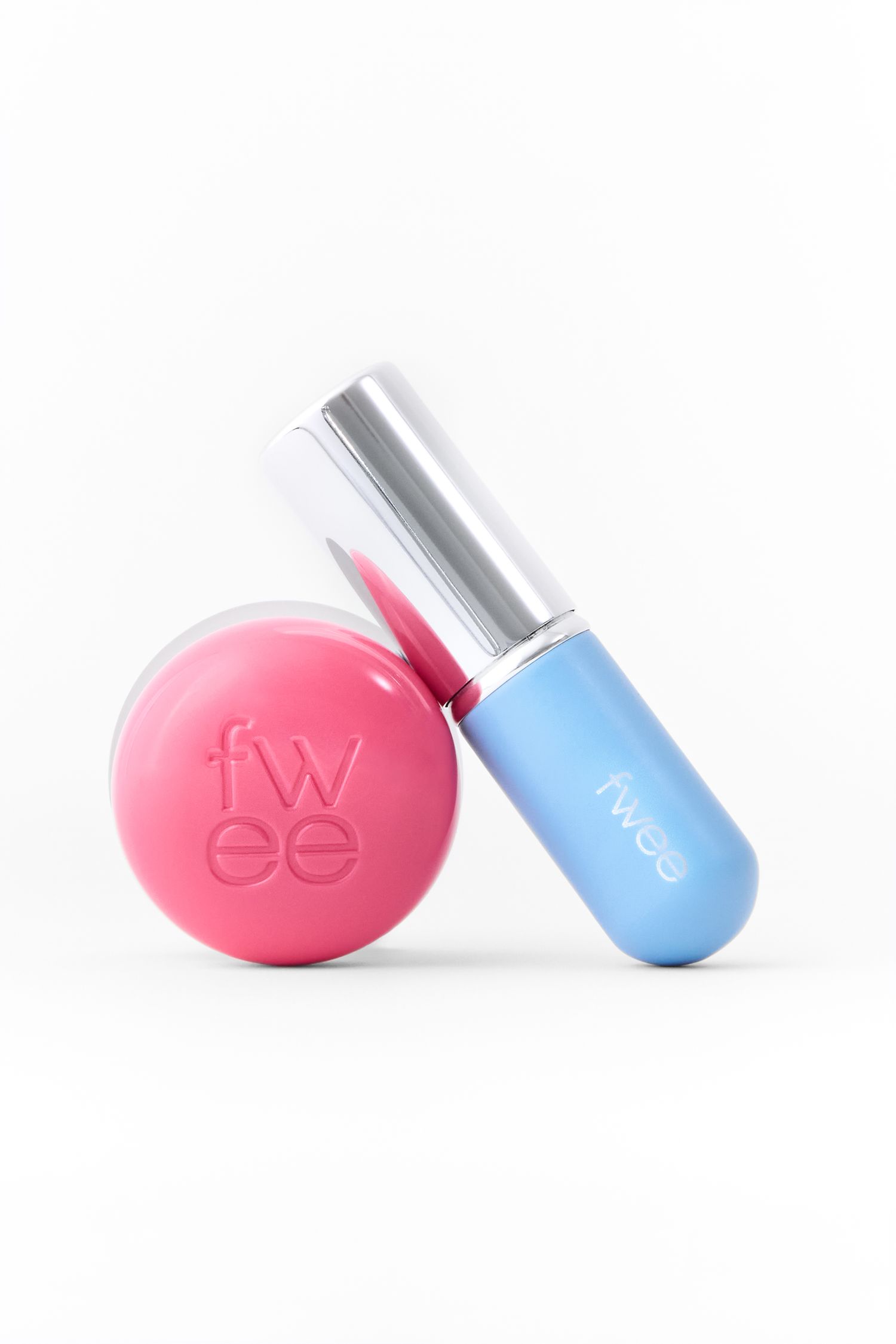 Fwee brand pink lip balm compact and blue lip gloss tube with silver cap on white background.