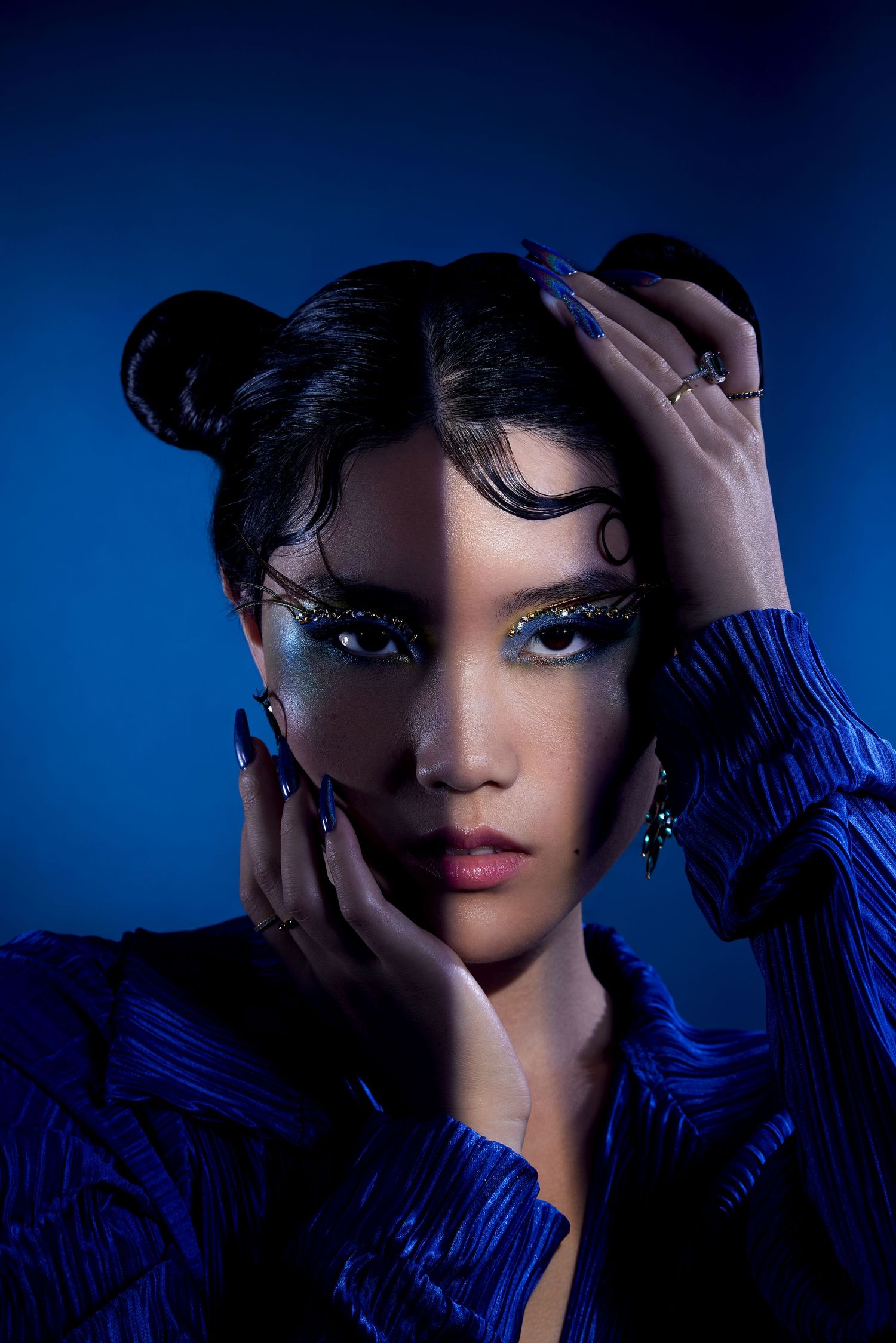 A dramatic fashion portrait series in deep blue lighting shows close-up beauty shots with striking makeup and styling.