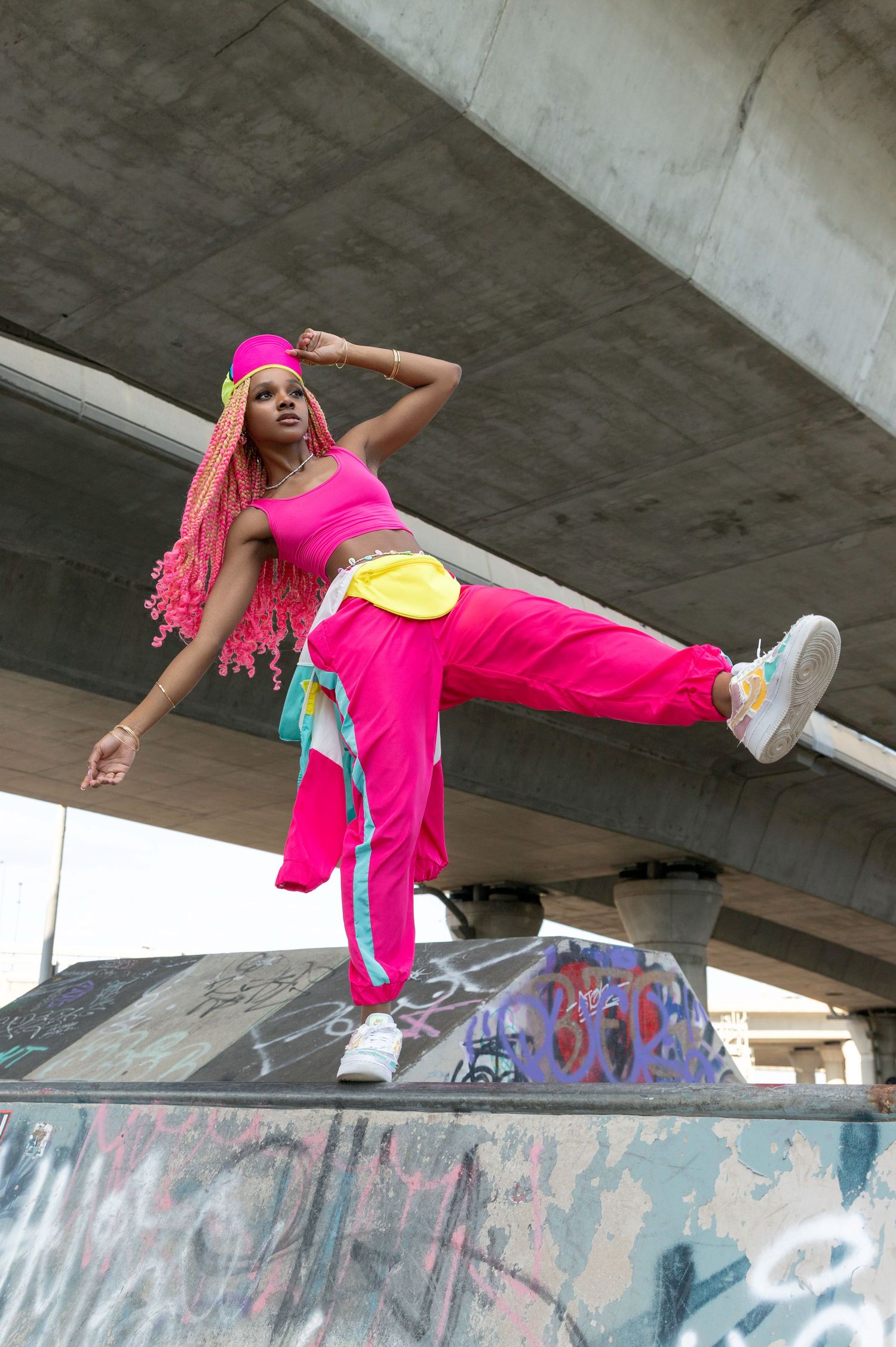Parkour athlete in vibrant pink outfit performs dynamic aerial movements over graffiti-covered concrete structures.
