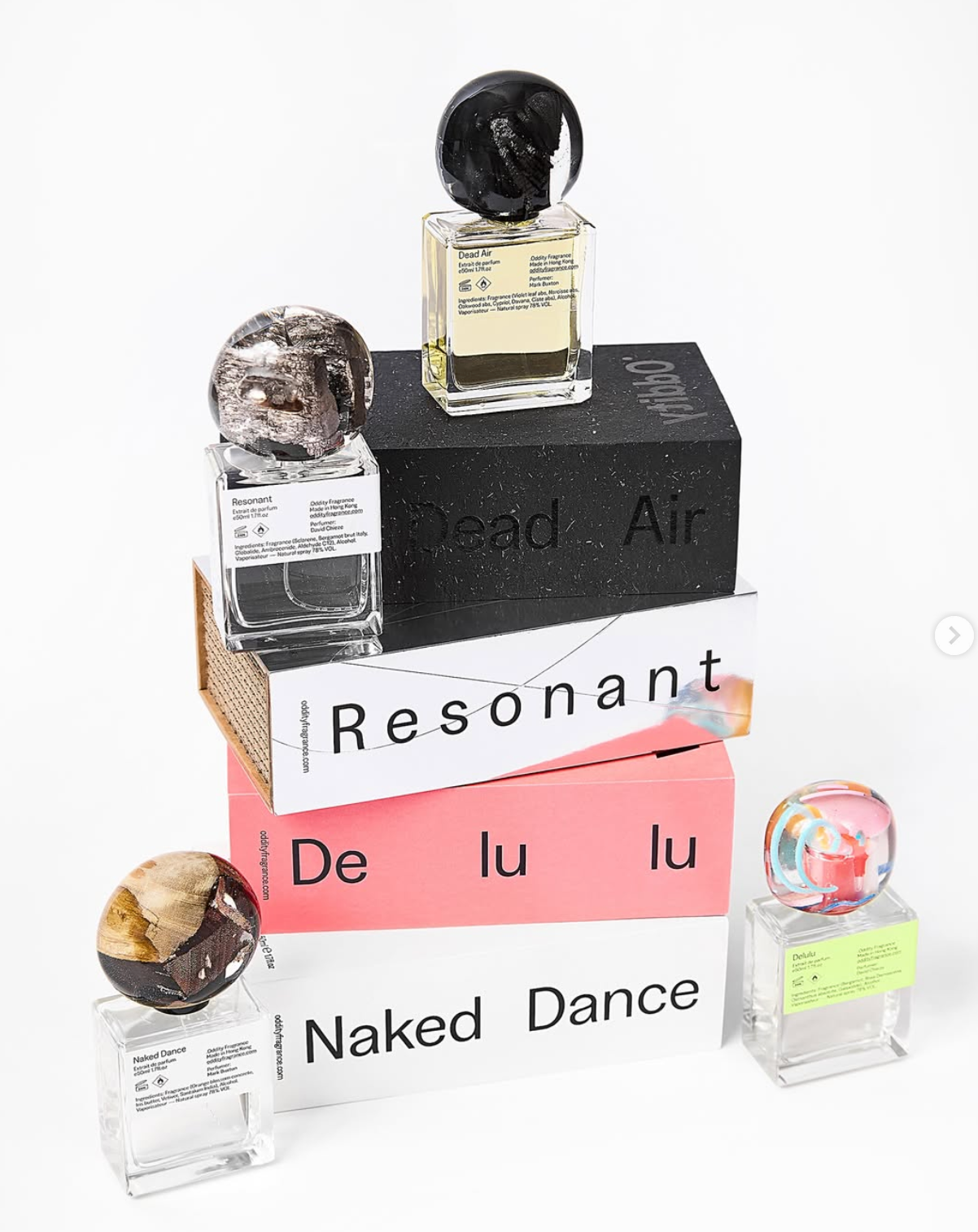 Four artisanal perfume bottles with sculptural glass caps stacked on boxes labeled Dead Air, Resonant, Delulu and Naked Dance.