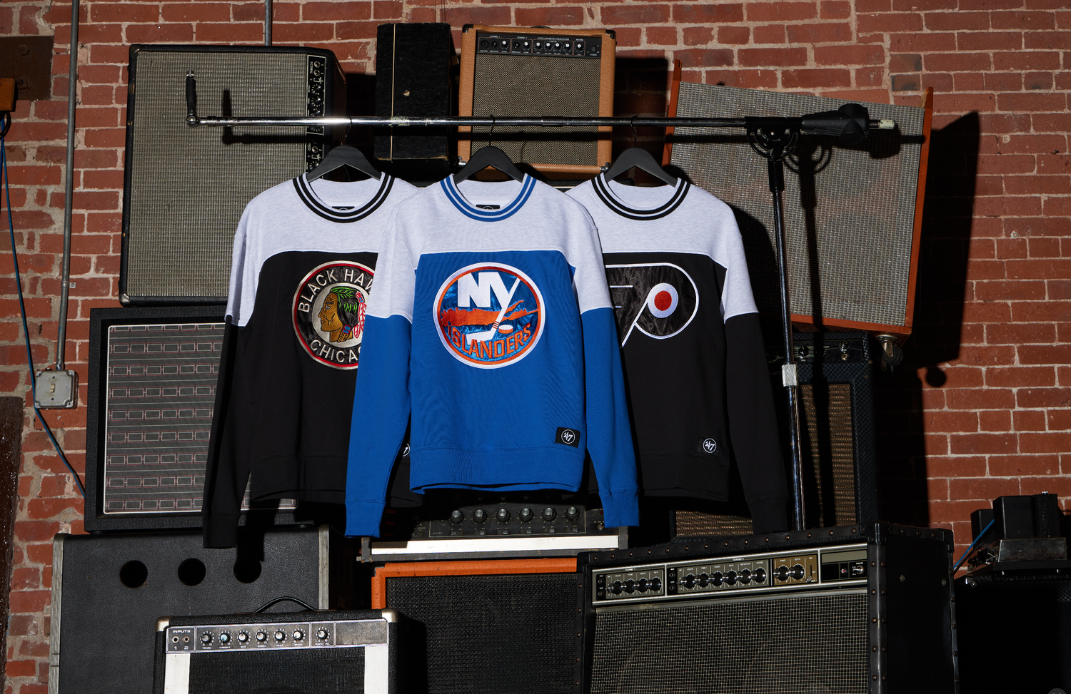 Three vintage hockey jerseys including a New York Islanders blue sweater displayed on hangers against a brick wall.