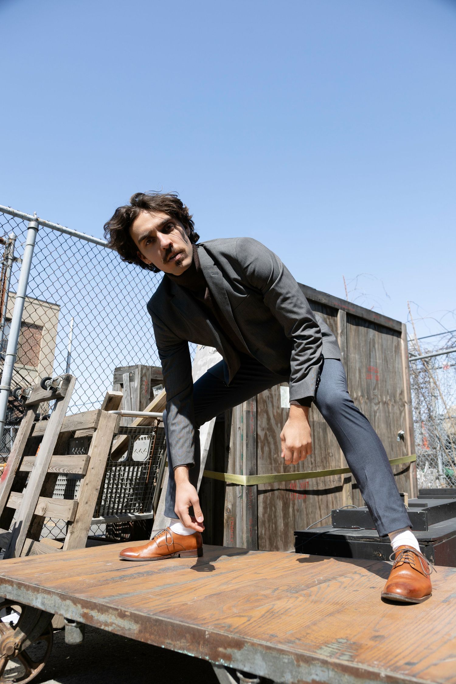 Low angle of a man dressed in a blazer and dress pants in an urban setting during a sunny day.