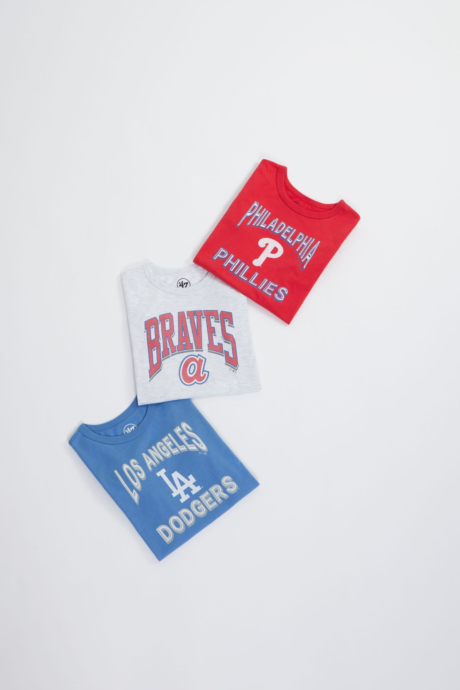 Baseball team merchandise featuring Braves, Phillies, and Dodgers sports apparel laid out on a white background.