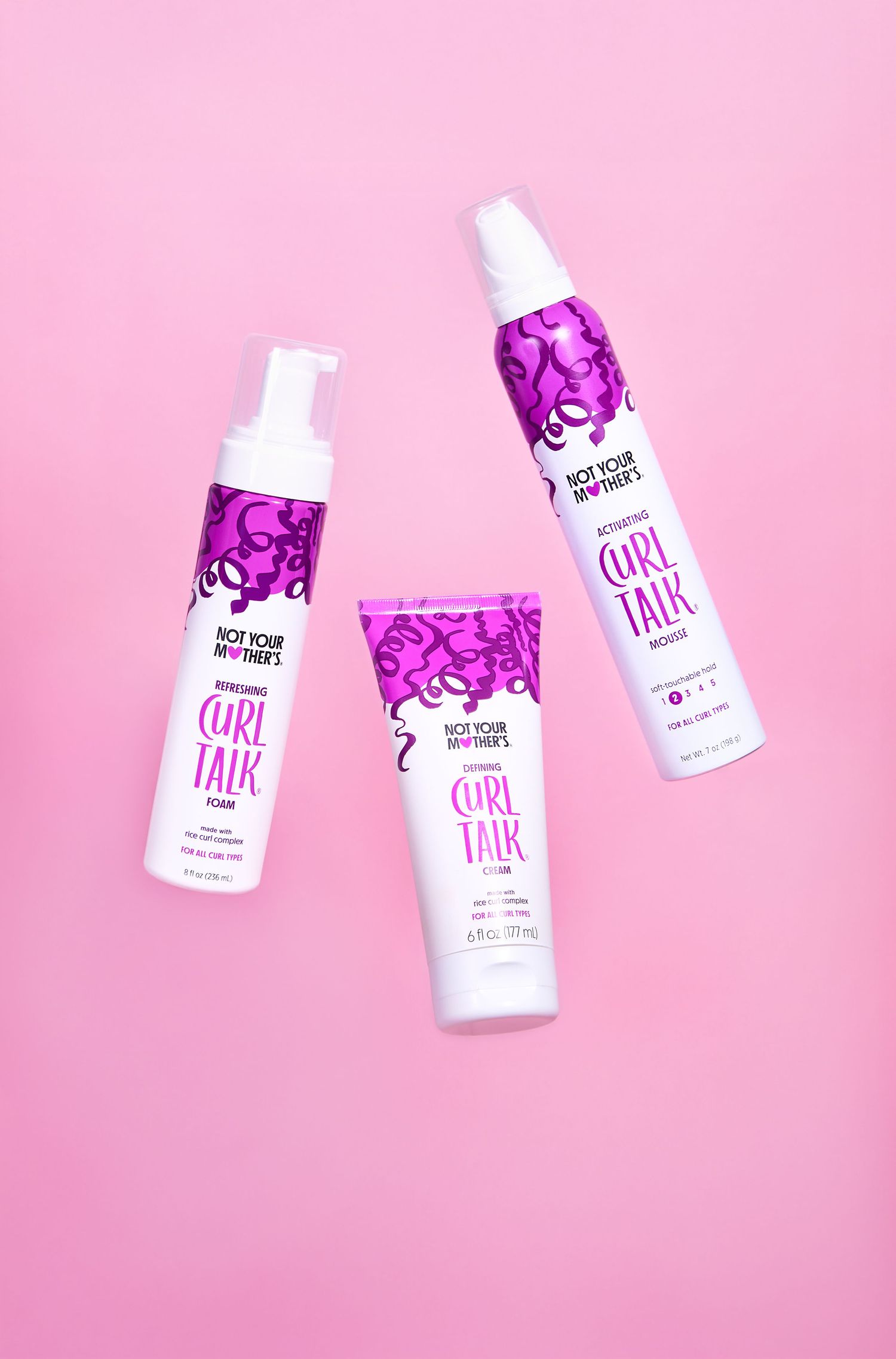 White cosmetic bottles with purple accents arranged diagonally on a pink background for beauty product photography.
