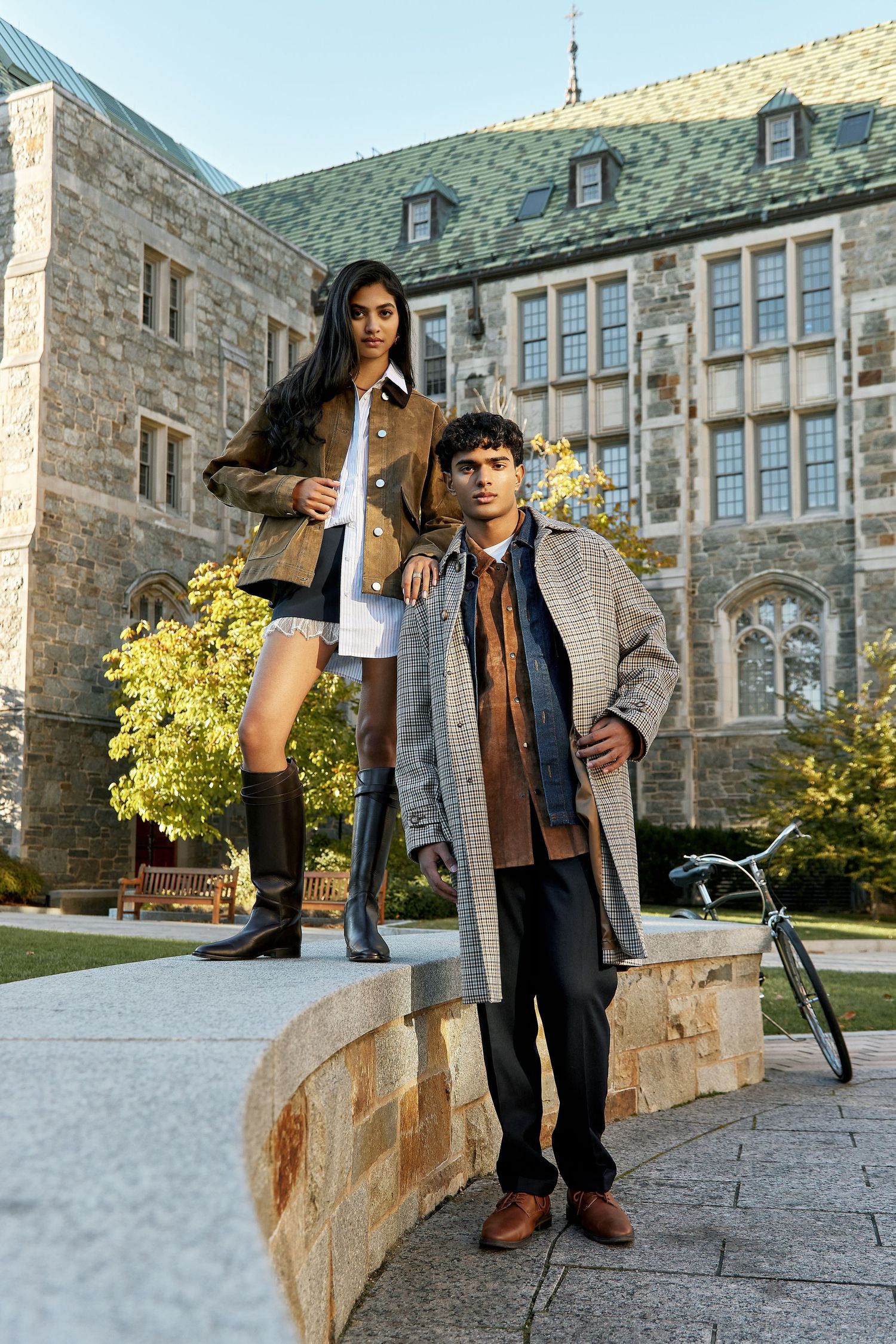 Two students posing on stone steps in front of a historic university building with gothic architecture.
