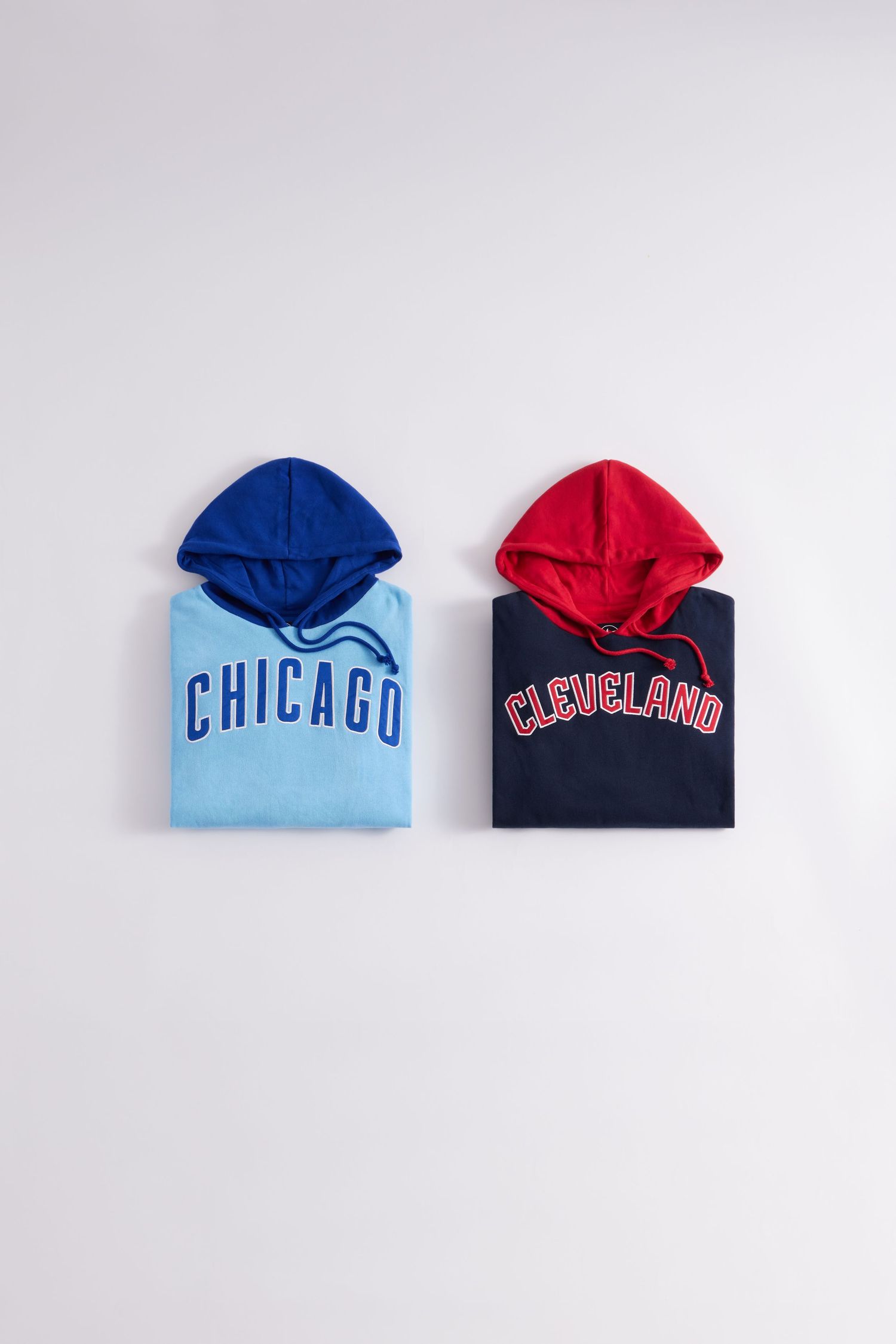 Folded hooded sweatshirts in blue and red with Chicago and Cleveland sports team branding laid flat on white surface.