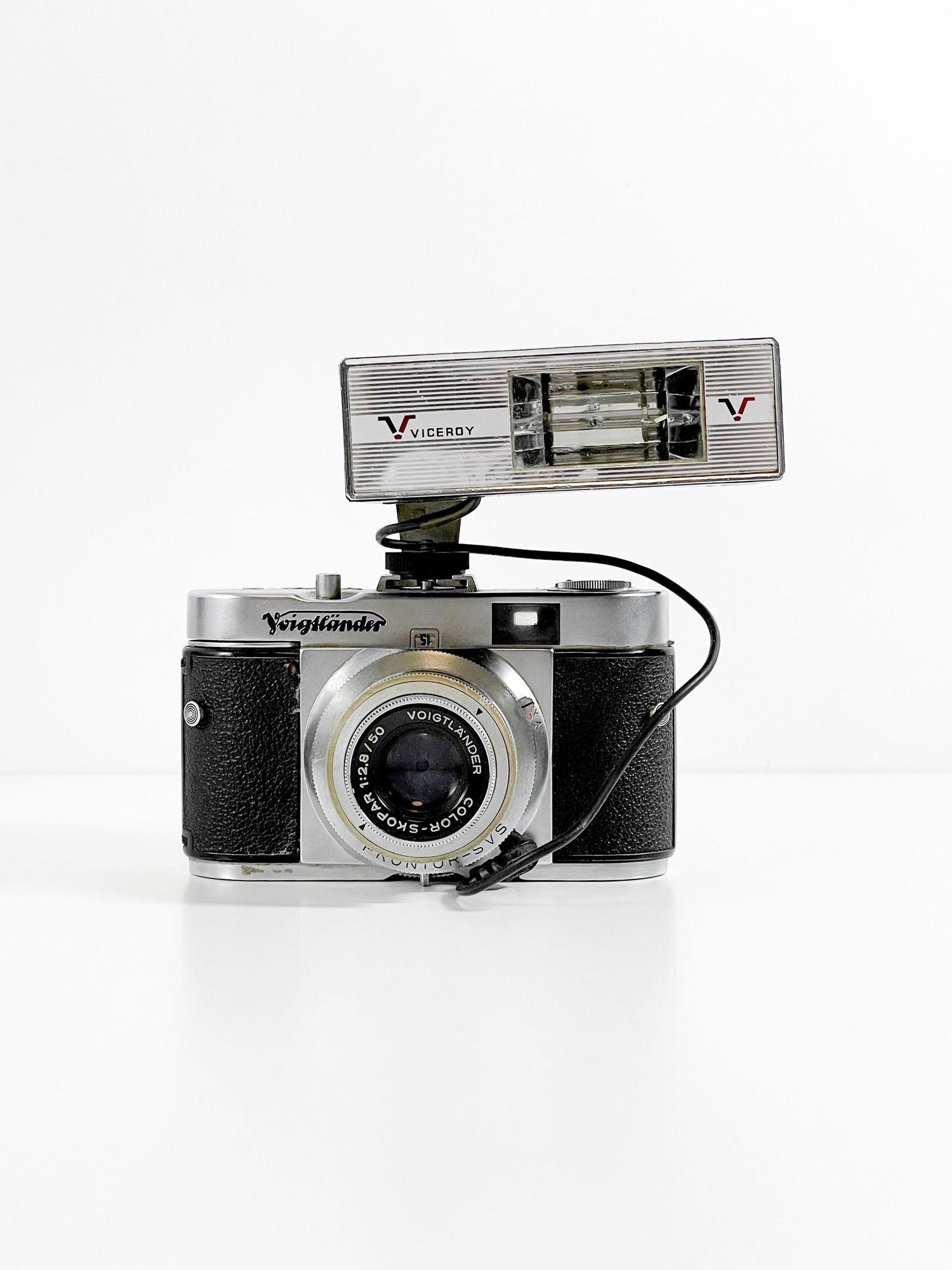 Vintage Voigtlander film camera with chrome lens and Vicency flash attachment on white background.