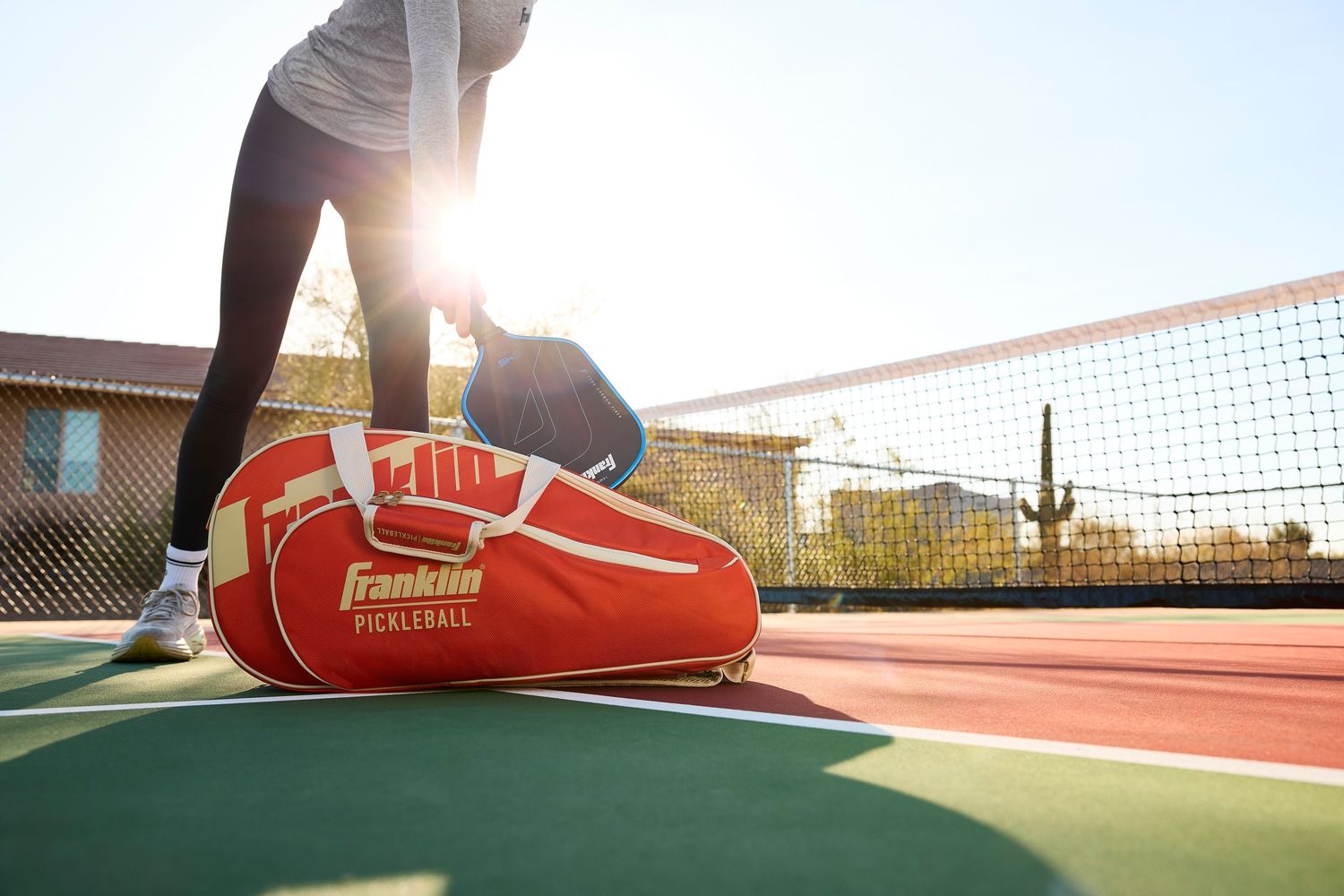 Athlete reaching for a Franklin Sports pickleball paddle on an outdoor pickleball court in AZ with the sun shining.