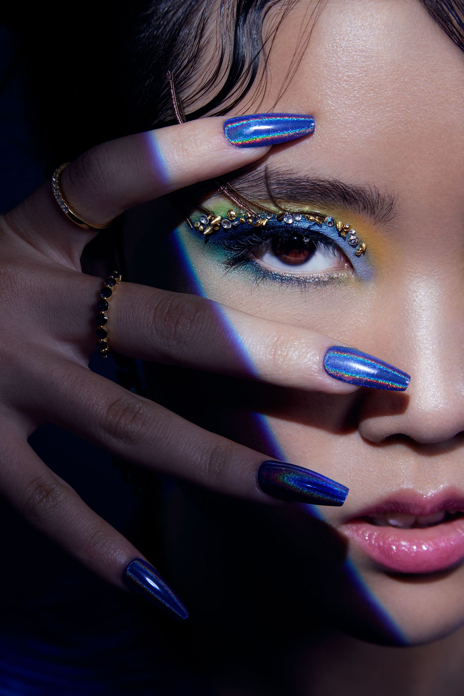 Close-up beauty shots featuring vibrant blue nail polish and metallic eyeshadow in dramatic lighting.