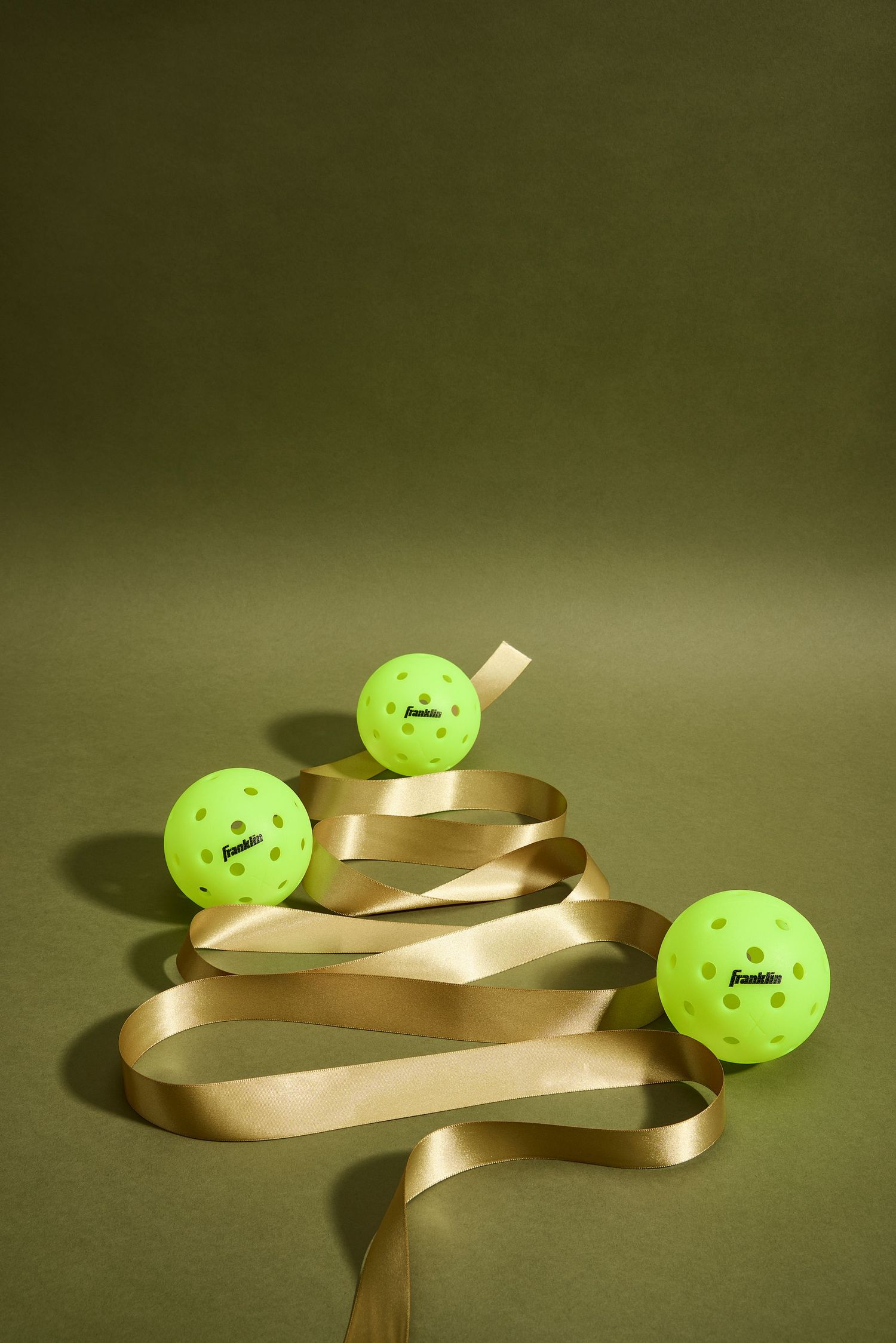Three bright neon green golf balls arranged with a spiraling gold ribbon against a dark green background.