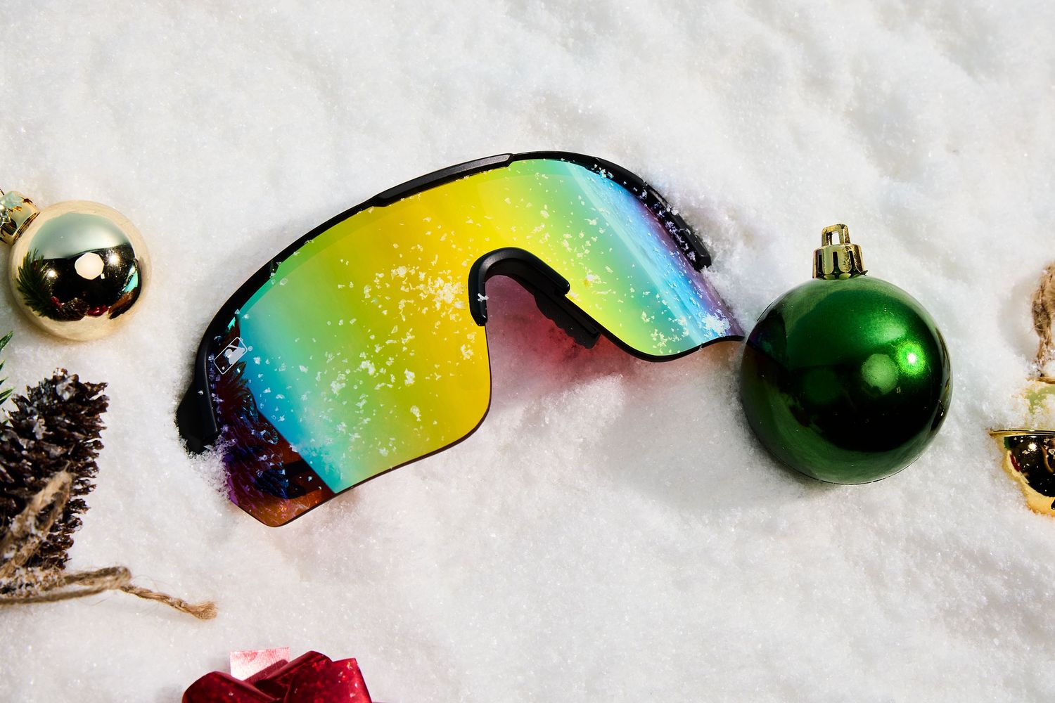 Colorful sunglasses and Christmas ornaments arranged in snow creating a festive holiday display.