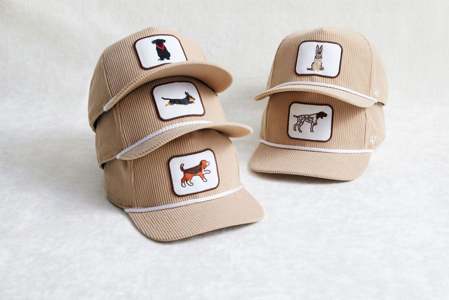 Five beige baseball caps with animal logo patches displayed in different angles on white background.