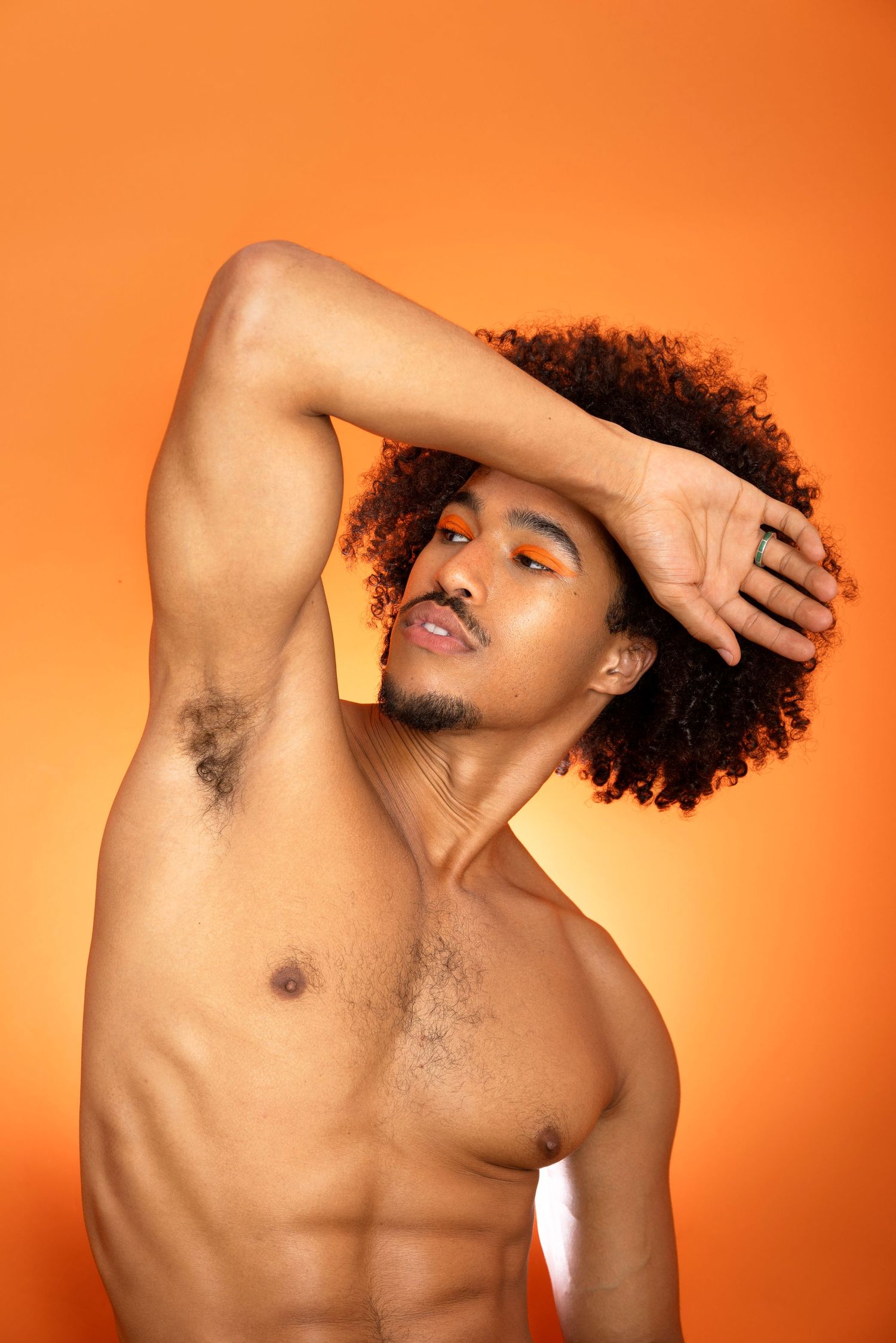 A shirtless person with curly hair poses against an orange backdrop in a dynamic fashion series.