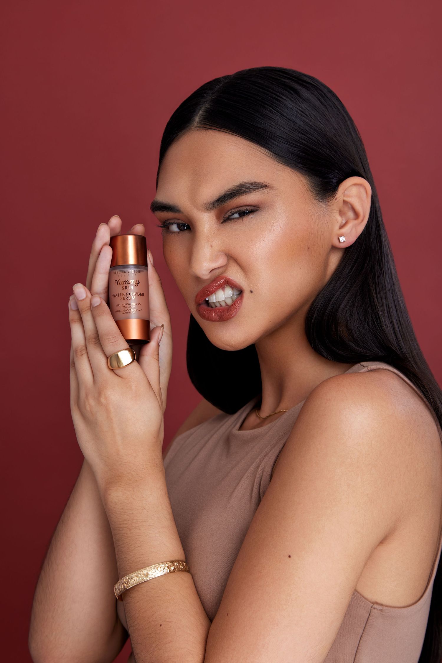 Beauty product advertisement showing model holding cosmetic bottle against burgundy background.