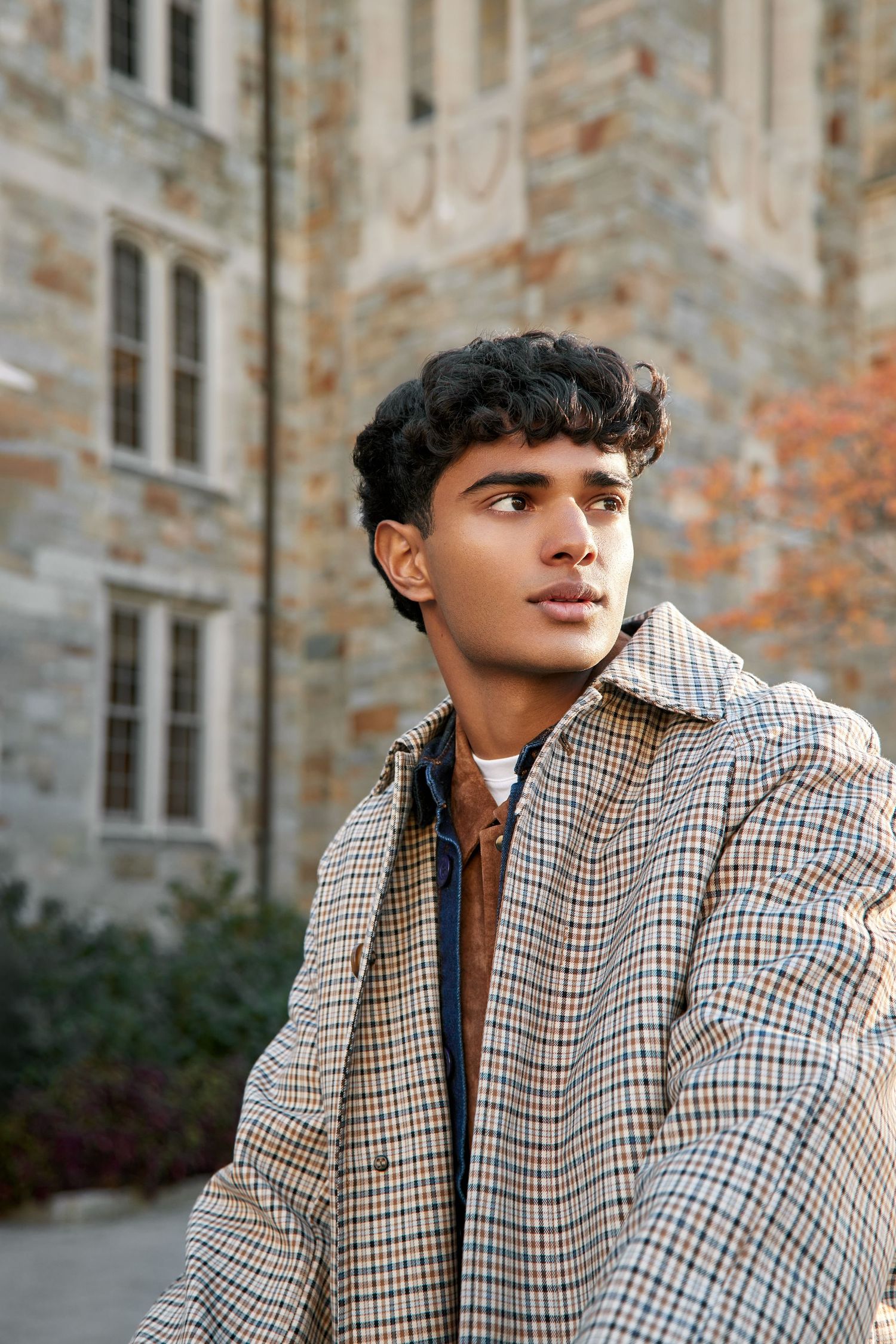 Fashion model wearing a stylish brown and white checkered blazer poses against stone building exterior.
