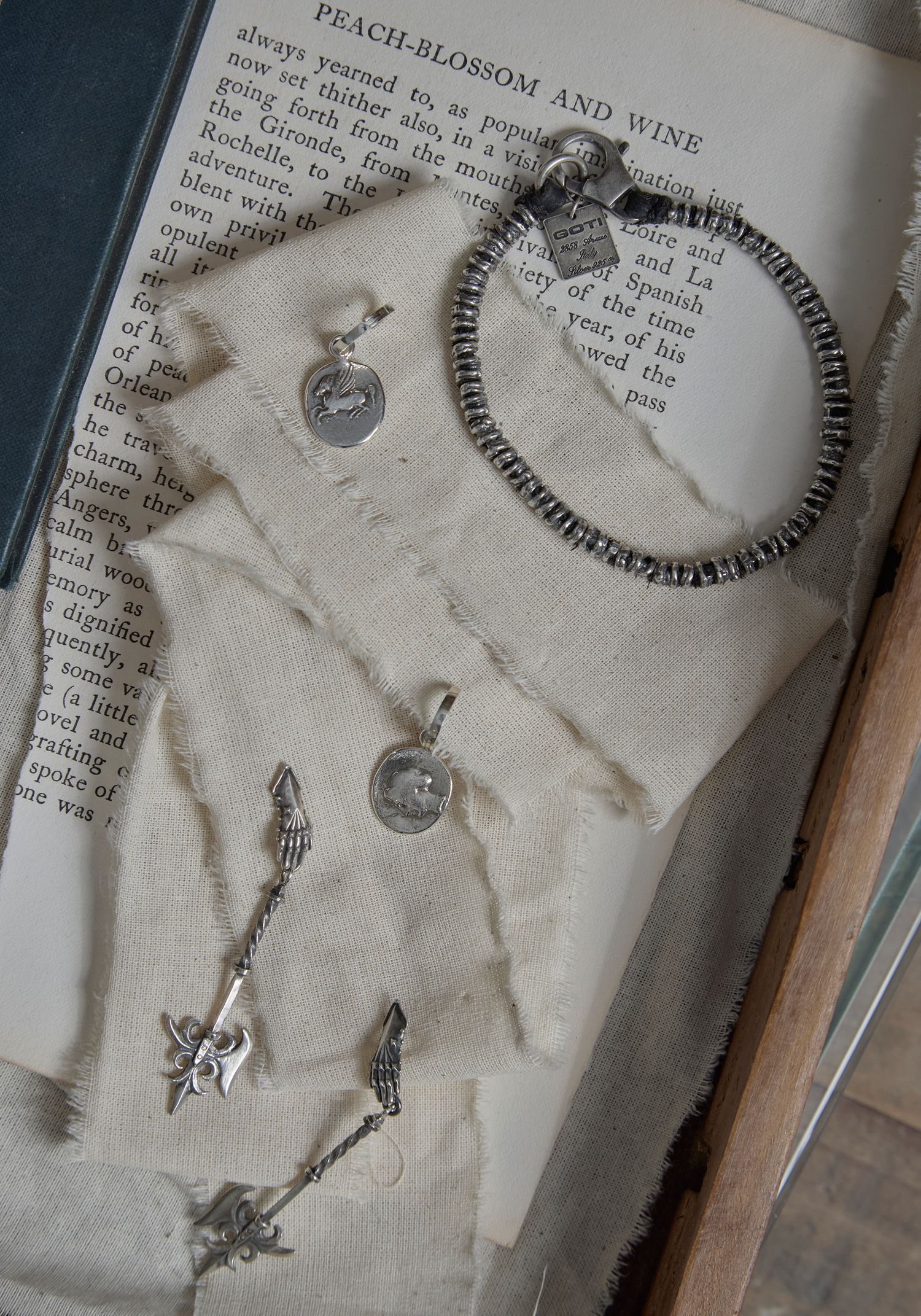 Silver jewelry collection including a bracelet, pendants, and charms displayed on an open vintage book page.