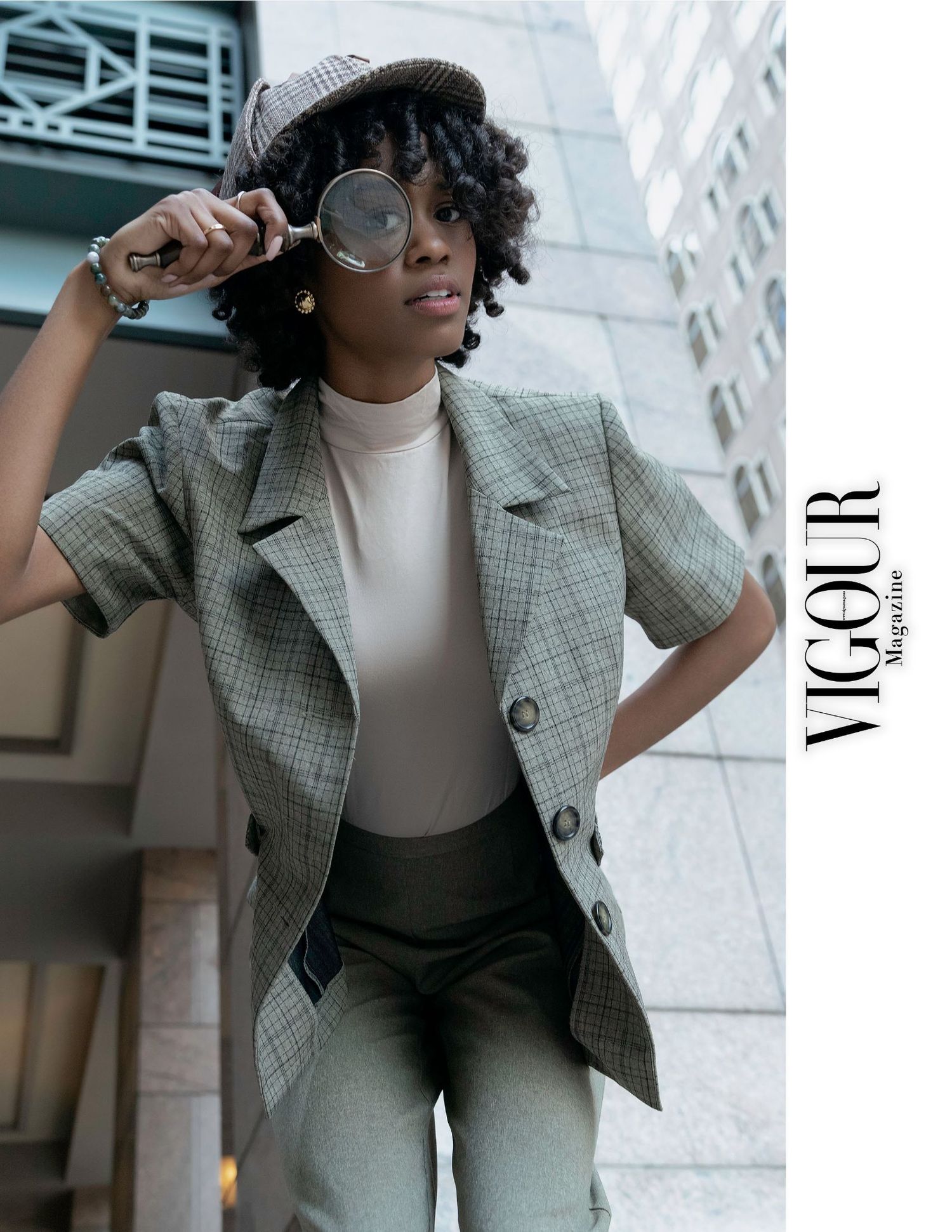 Woman in a plaid blazer and sunglasses poses confidently against a modern architectural backdrop featured in Vigour Magazine.