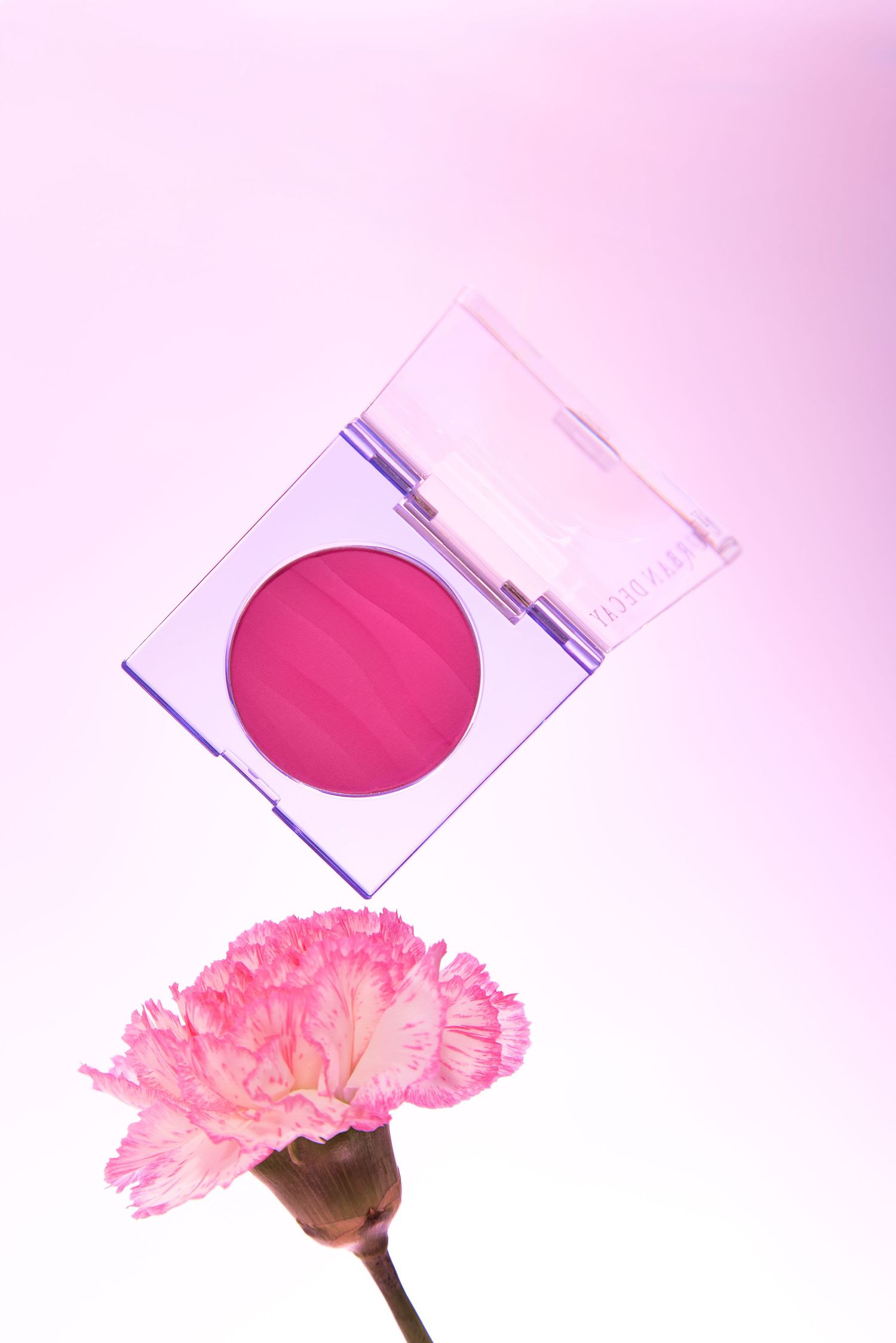 Pink blush compact makeup palette floating above a pink carnation flower on a soft pink background.