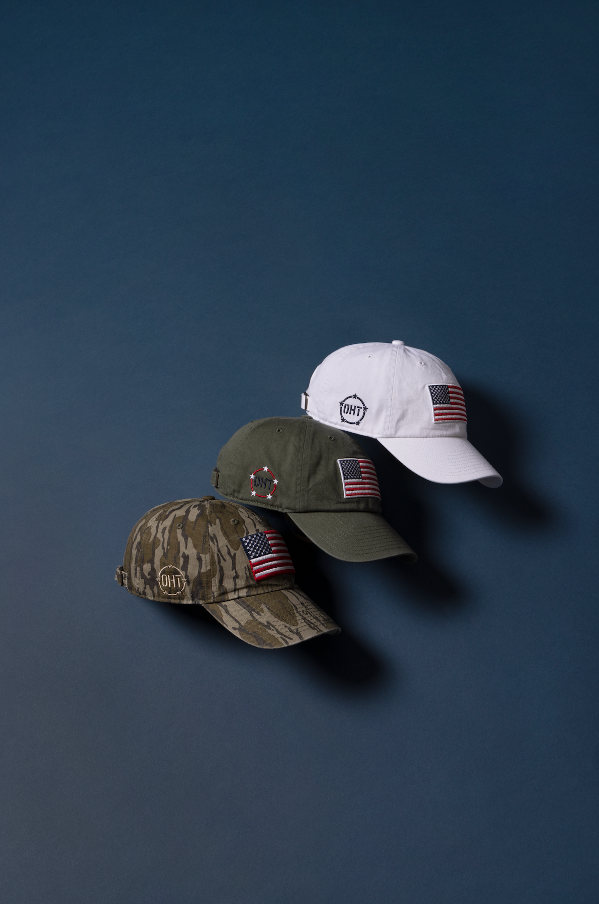 Three baseball caps with American flag patches arranged in a row against a dark blue background.