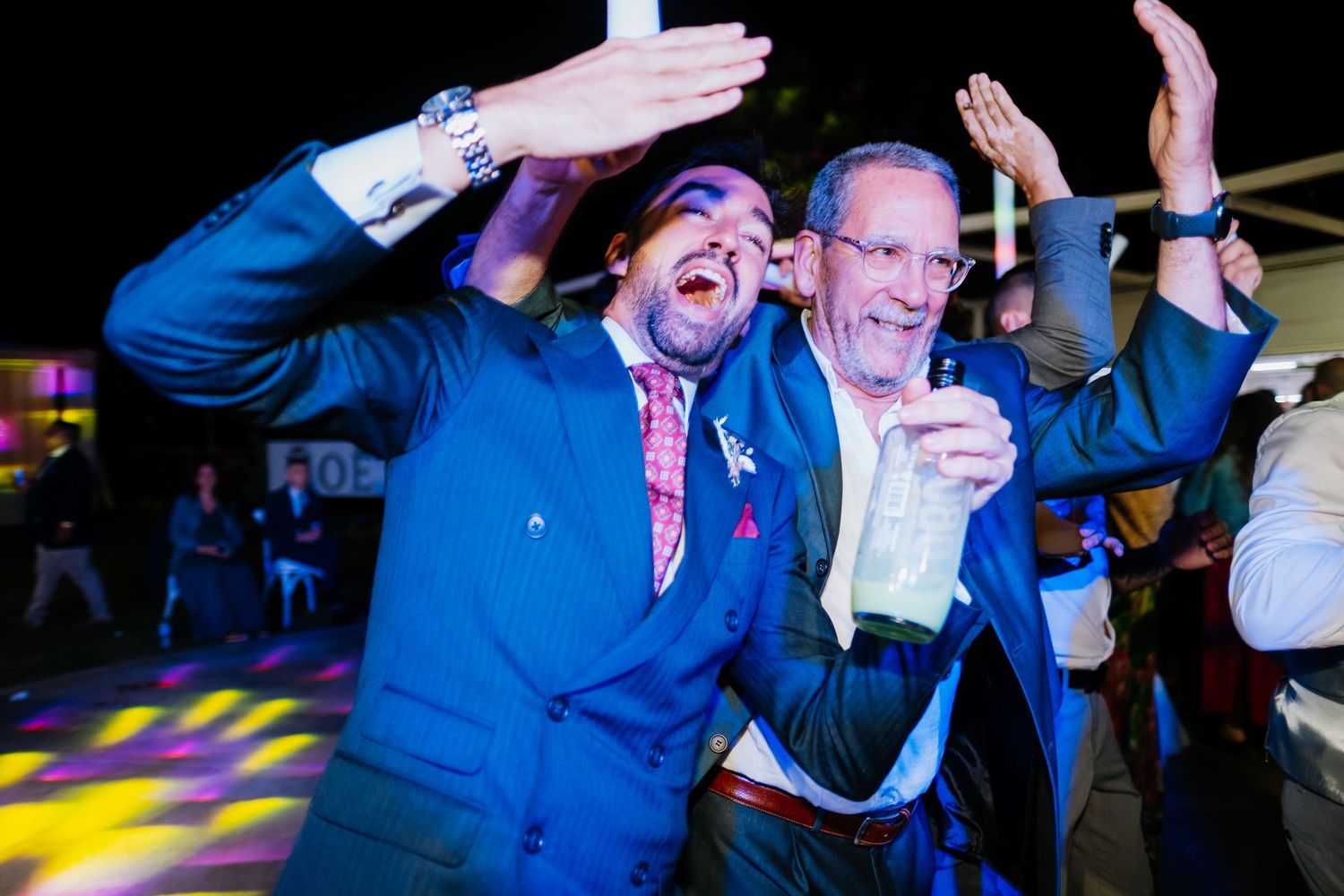 Energetic dance party with guests celebrating under blue and purple lighting.