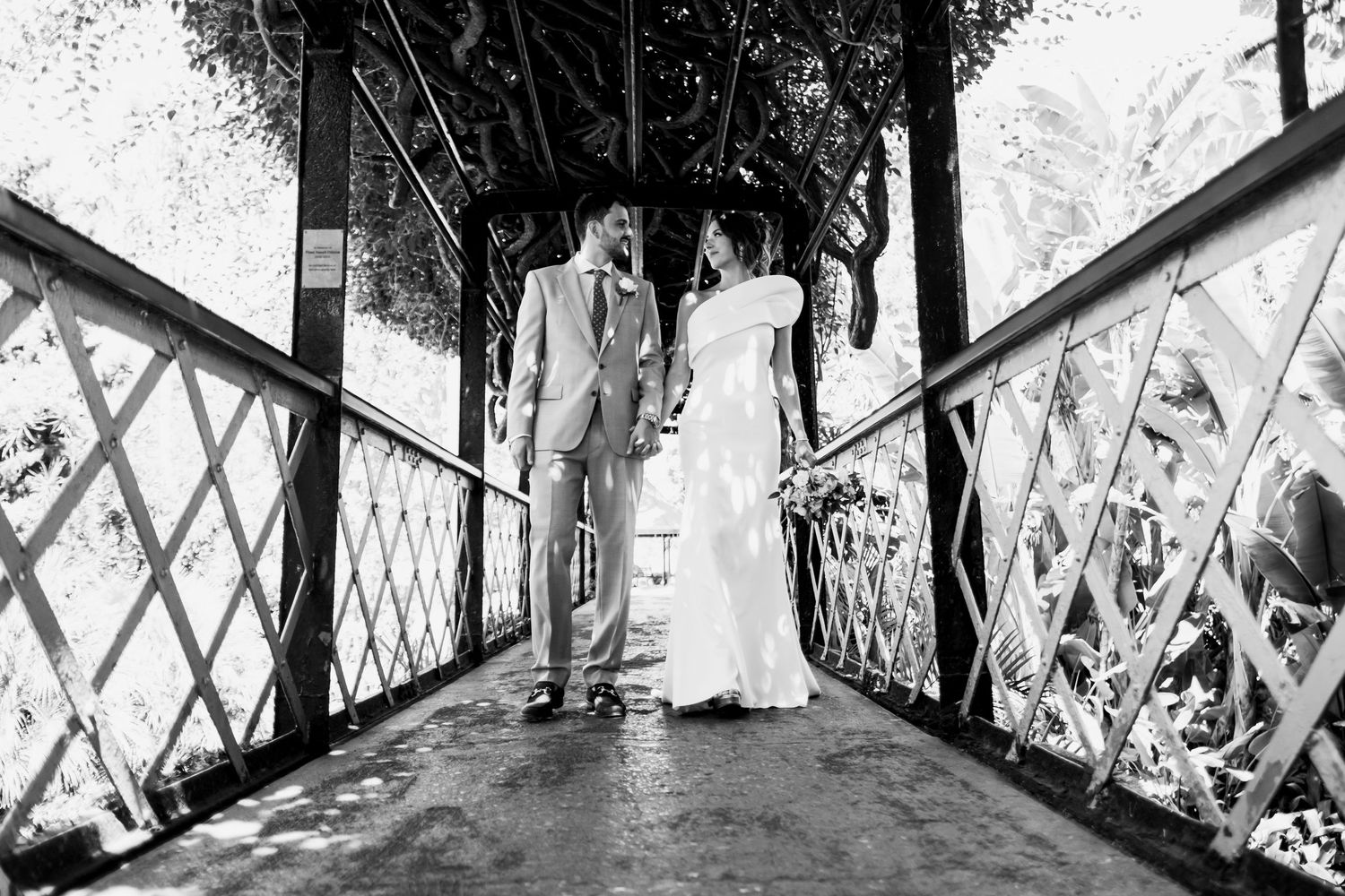 Black and white panoramic shot of people walking across a bridge or walkway.