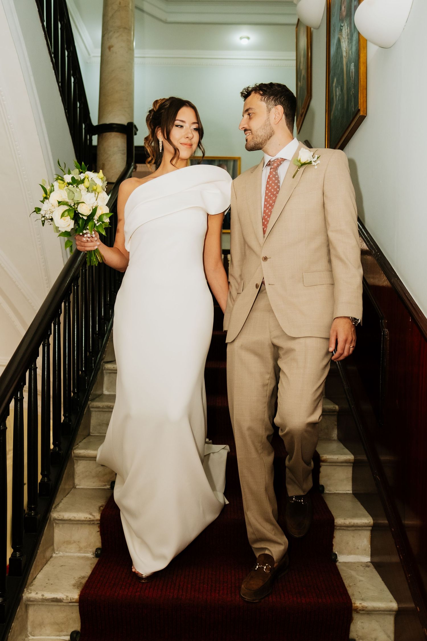Couple descending grand staircase in formal wedding attire with white dress and tan suit.