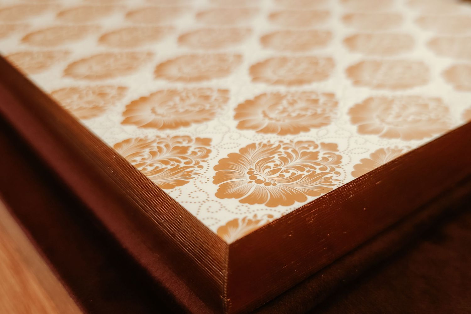 Close-up of wooden table corner with vintage beige floral damask pattern on the surface.