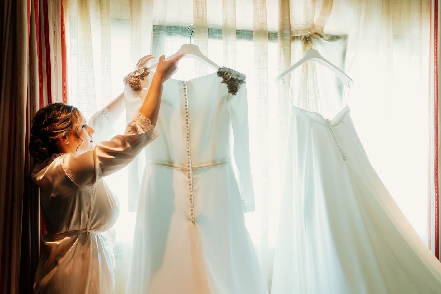 Vestido de novia de alta costura de Franc Sarabia colgado a contraluz en habitación de hotel en Córdoba, fotografía de preparativos elegante