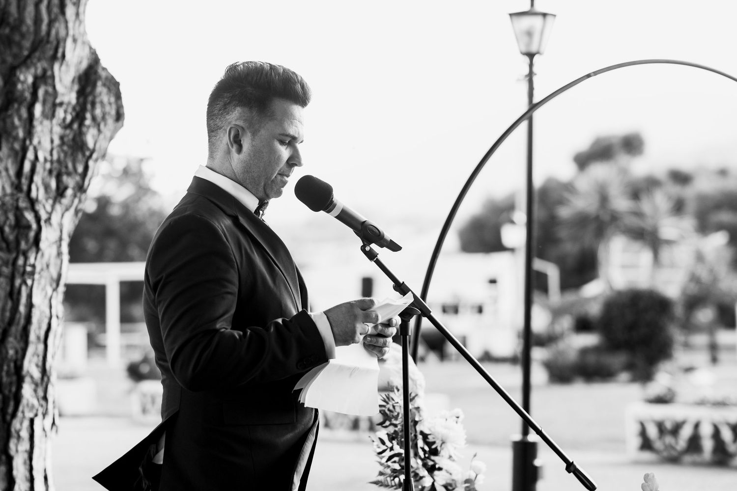 A black and white photo shows musicians performing on stage with instruments and microphones at an outdoor venue.