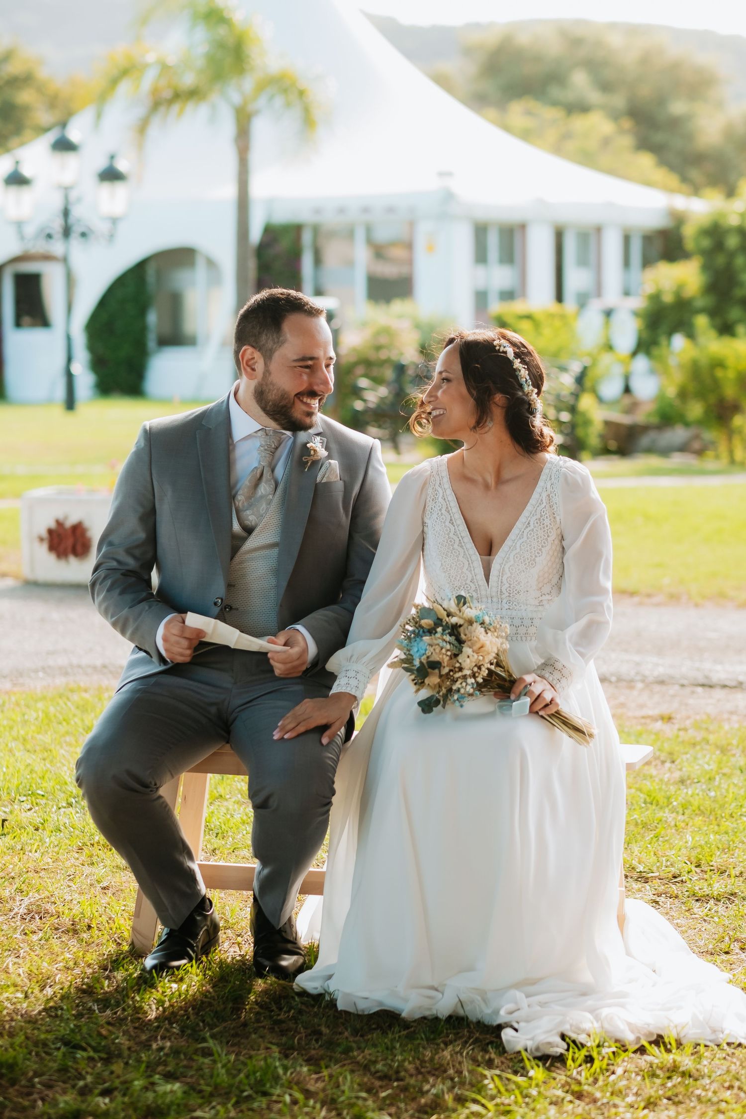 Newlyweds share a joyful moment sitting together outdoors at their garden wedding venue.