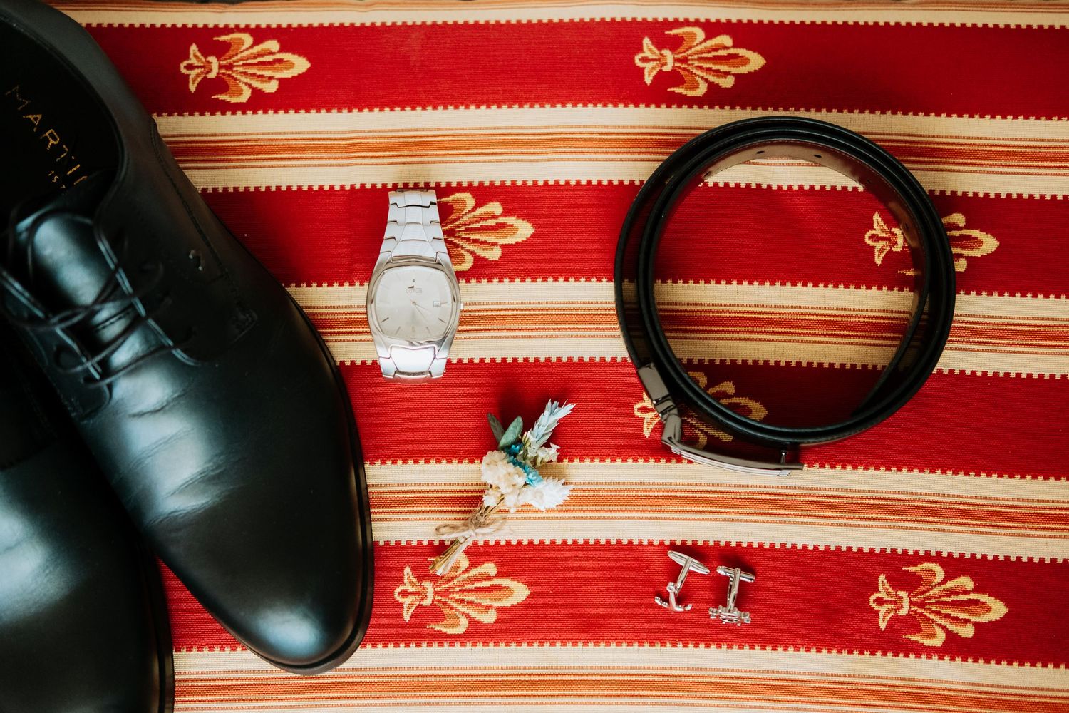 Black leather dress shoes and accessories arranged on a red and gold striped fabric.