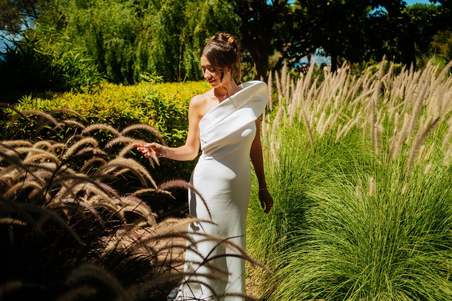 Wedding couple walking through garden path surrounded by tall ornamental grasses.