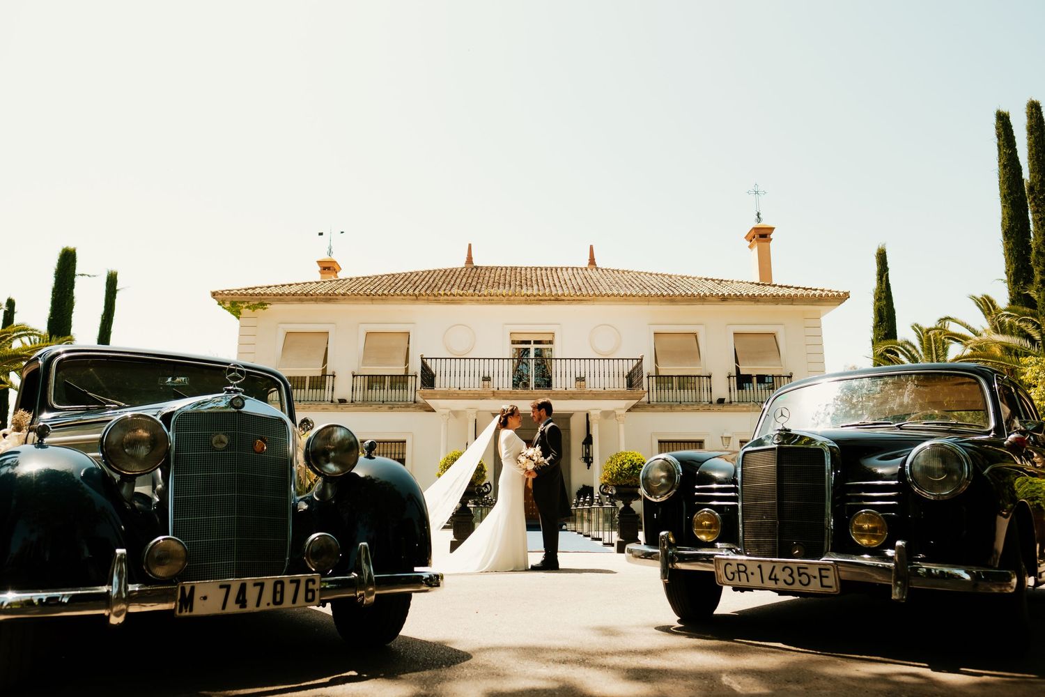 Novios posando junto a los coches oficiales para boda
