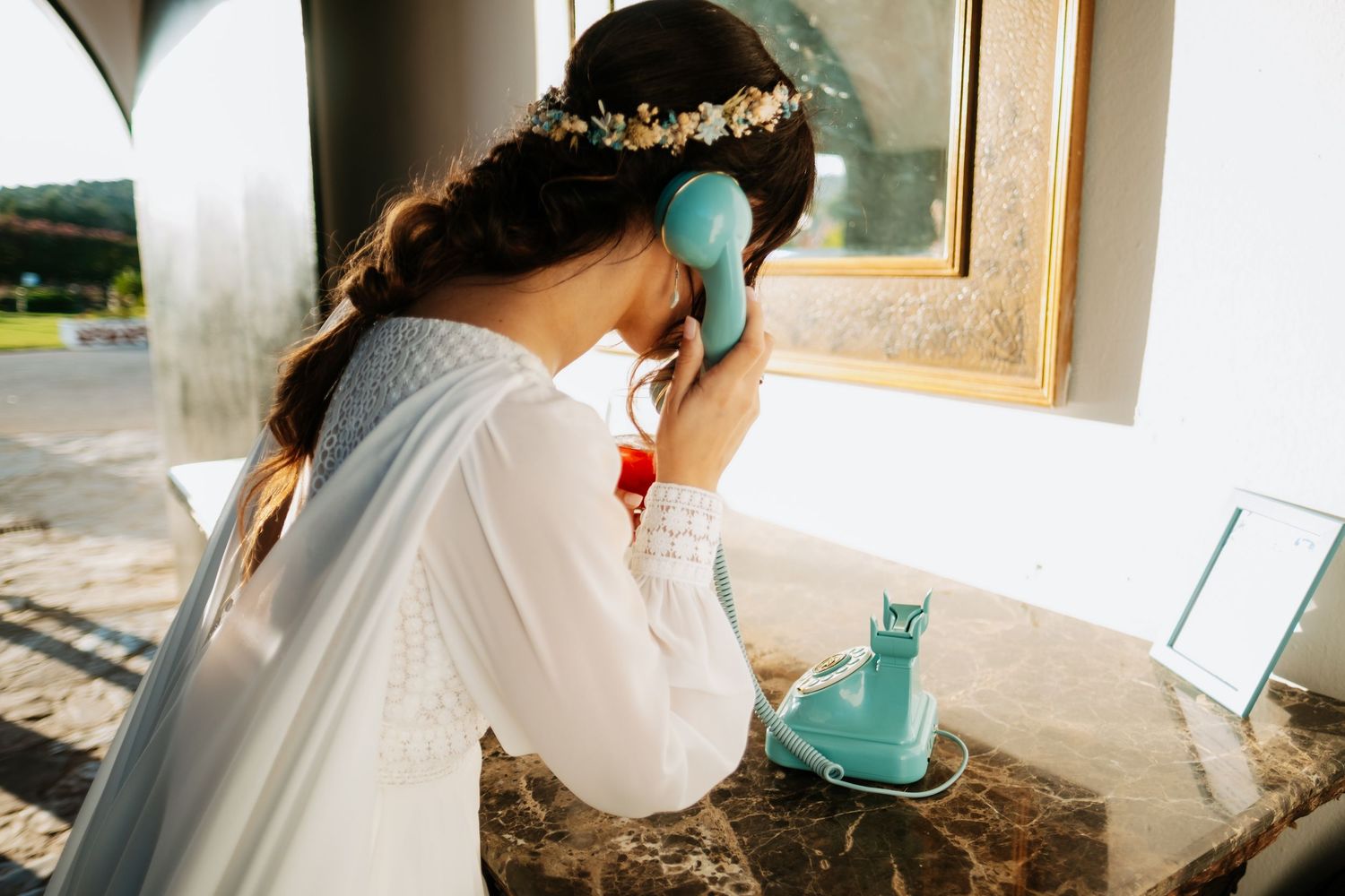 Bride preparing for wedding day with turquoise accessories near a window.