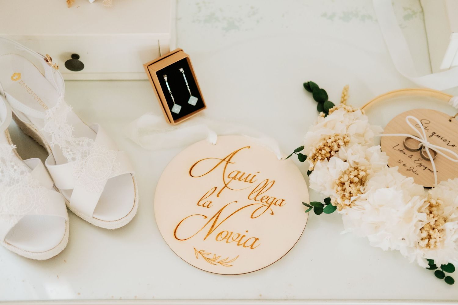 Elegant wedding details including place cards, earrings, and white floral decorations arranged on a light surface.